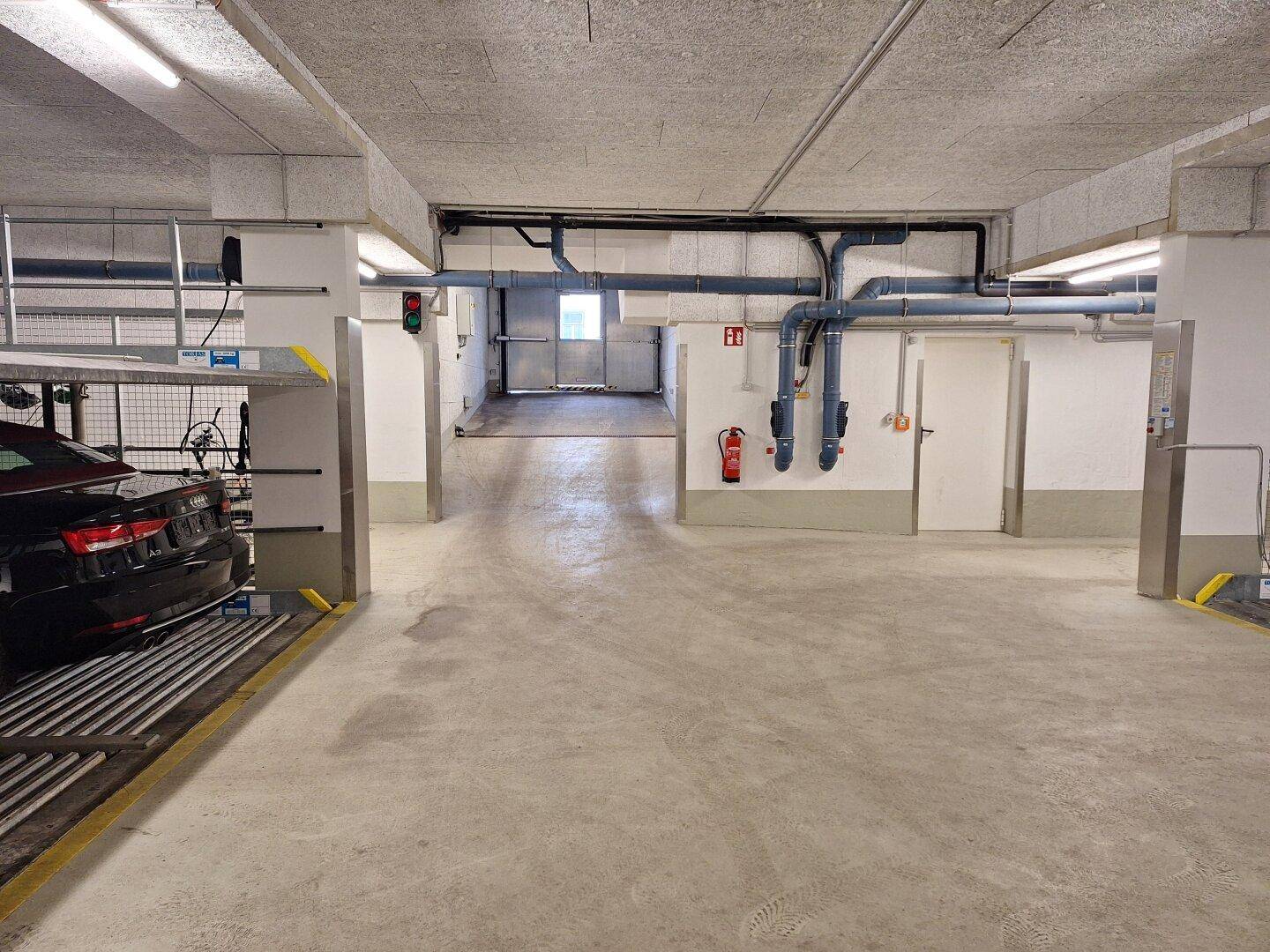 Geräumige Tiefgarage mit Betonboden, sichtbaren Installationen und weiteren Stellplätzen.