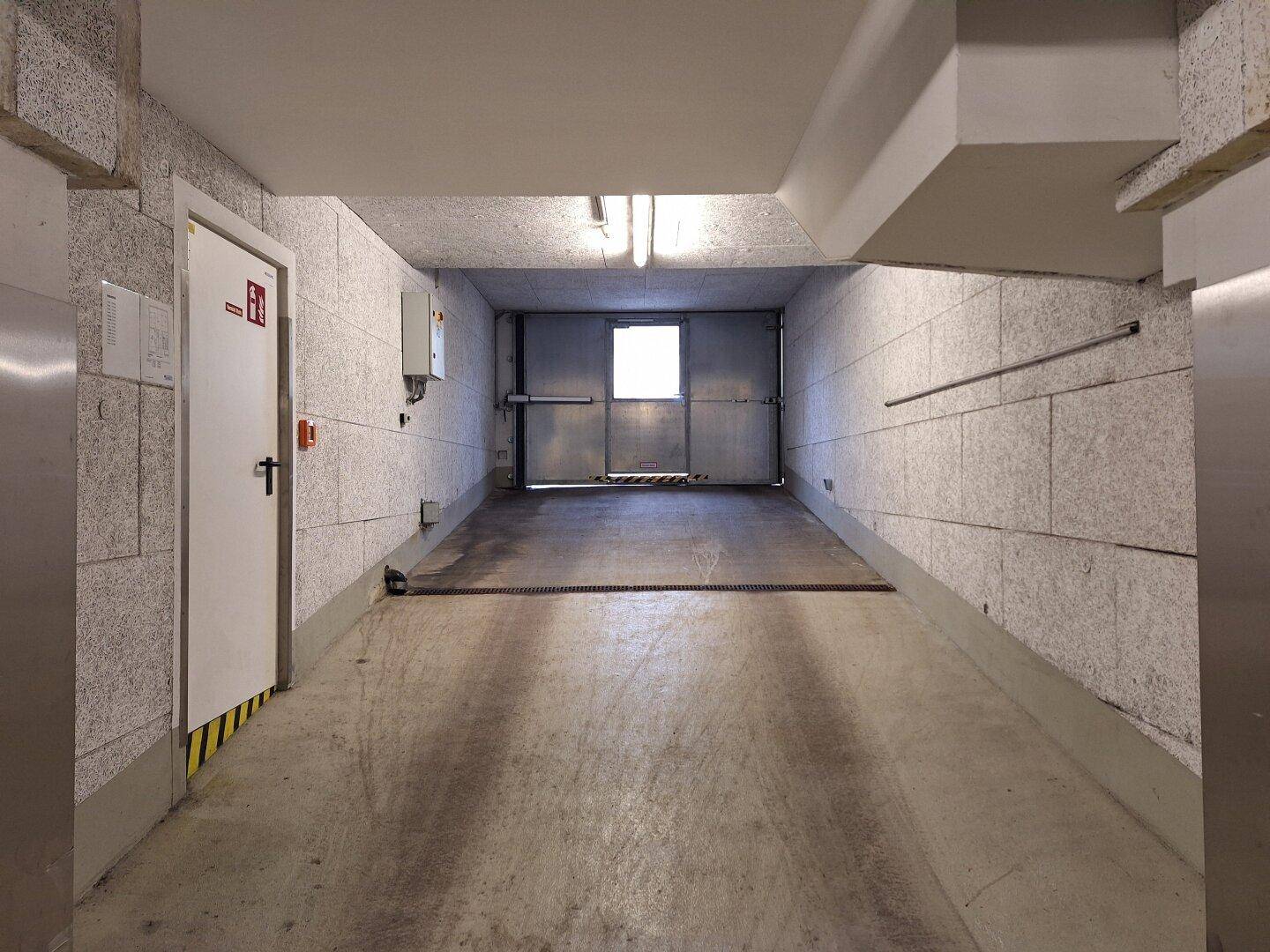 Zufahrt zur Tiefgarage mit Betonwänden, Rampe und Ausgangstür.