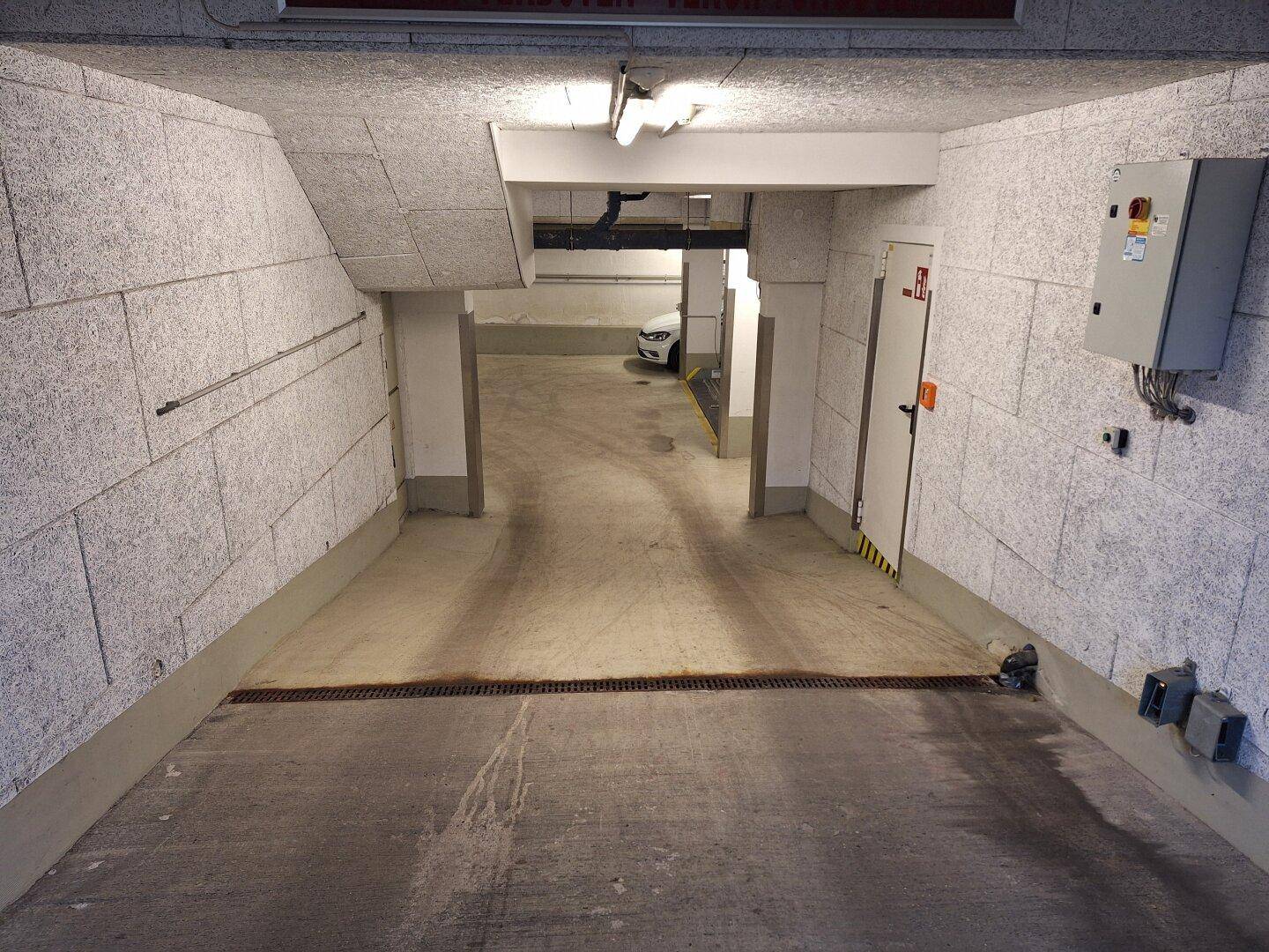 Einfahrt zur Tiefgarage mit geneigter Rampe und strukturierten Wänden aus einer anderen Perspektive.