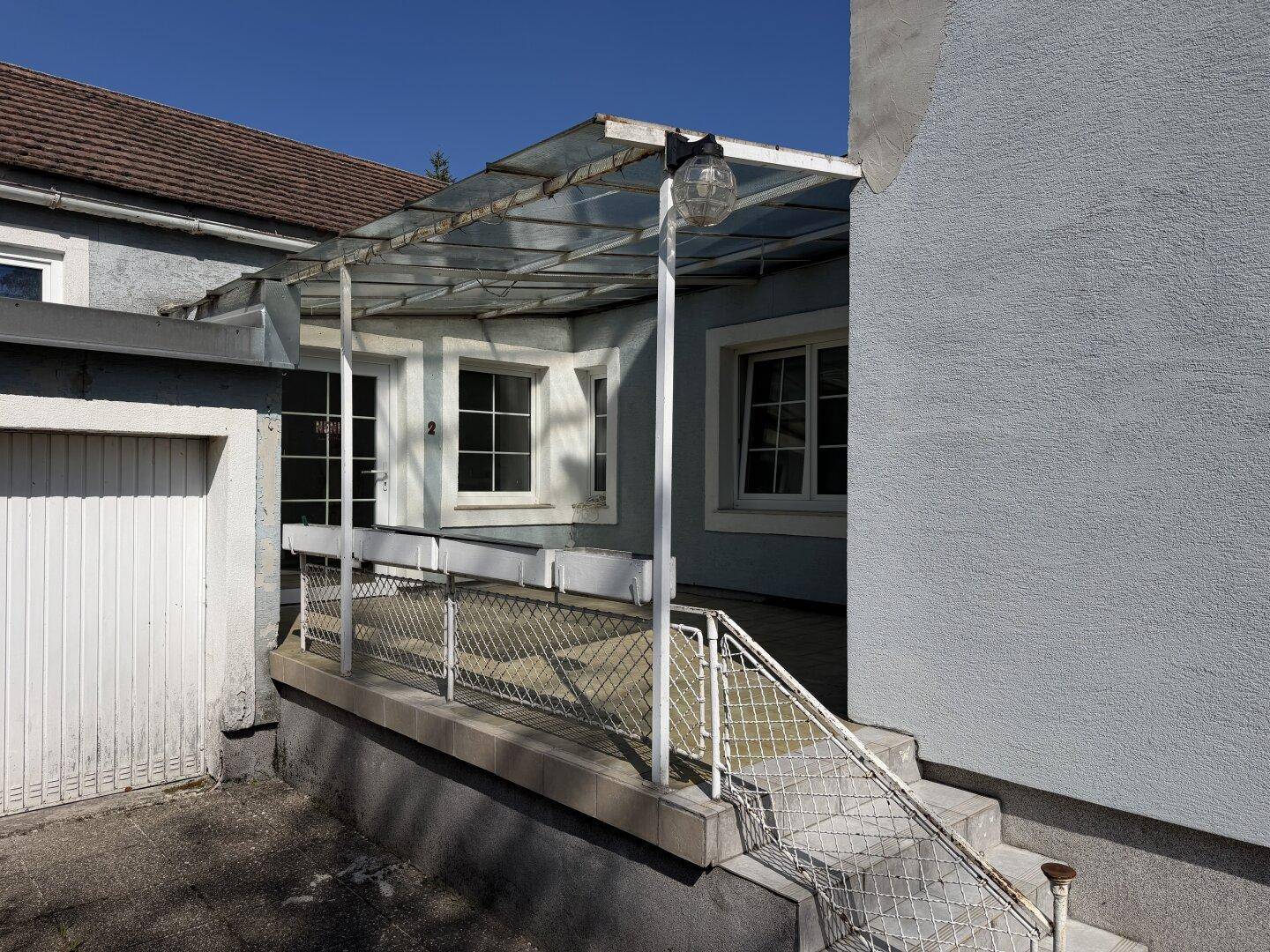 Überdachte Terrasse mit Fliesenboden und Zugang zum Haus und zur Garage.