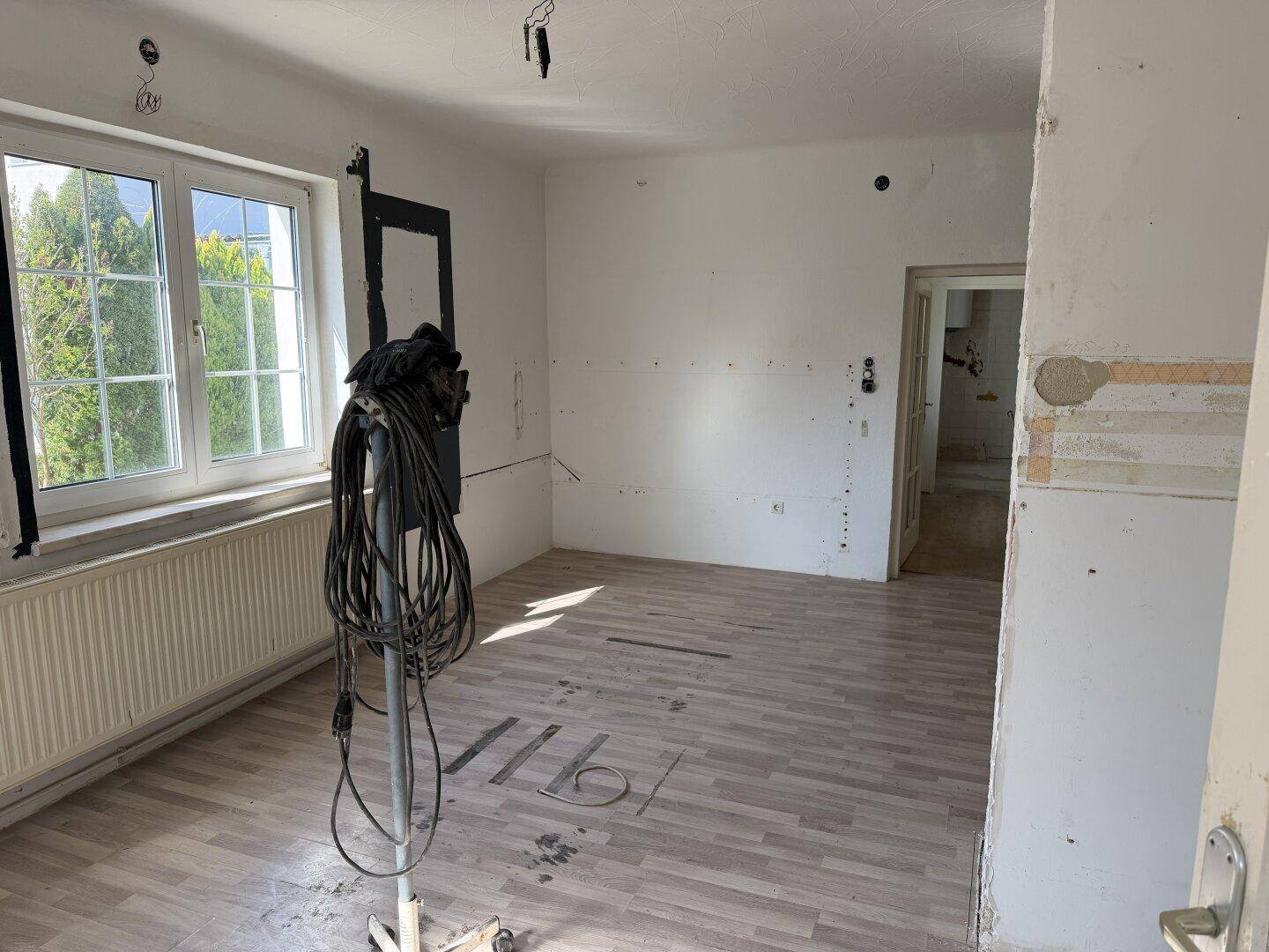 Geräumiger Wohnraum im Renovierungszustand mit großem Fenster und Laminatboden.