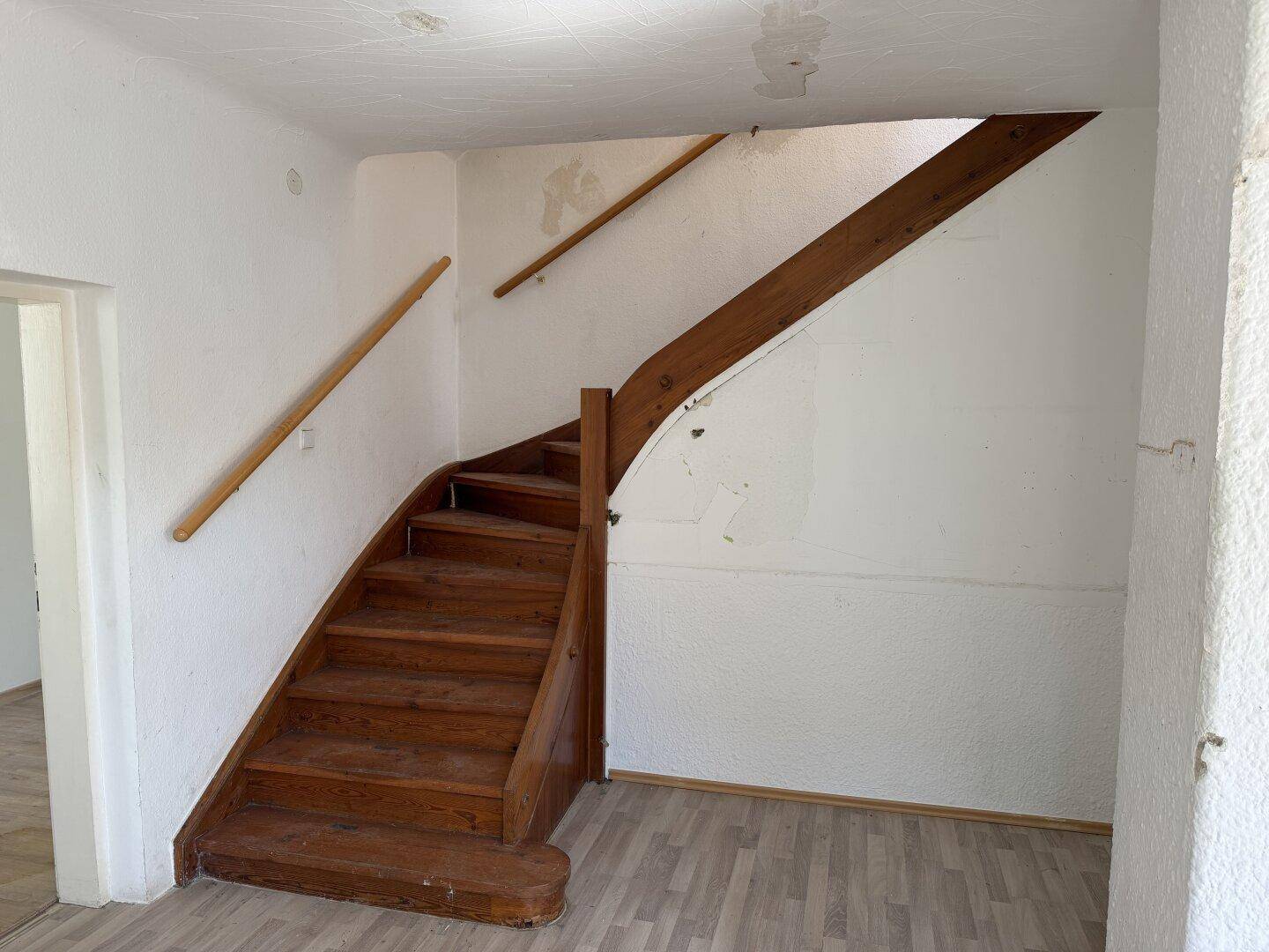 Treppenhaus mit Holztreppe und Handläufen, das in einem Renovierungszustand ist.