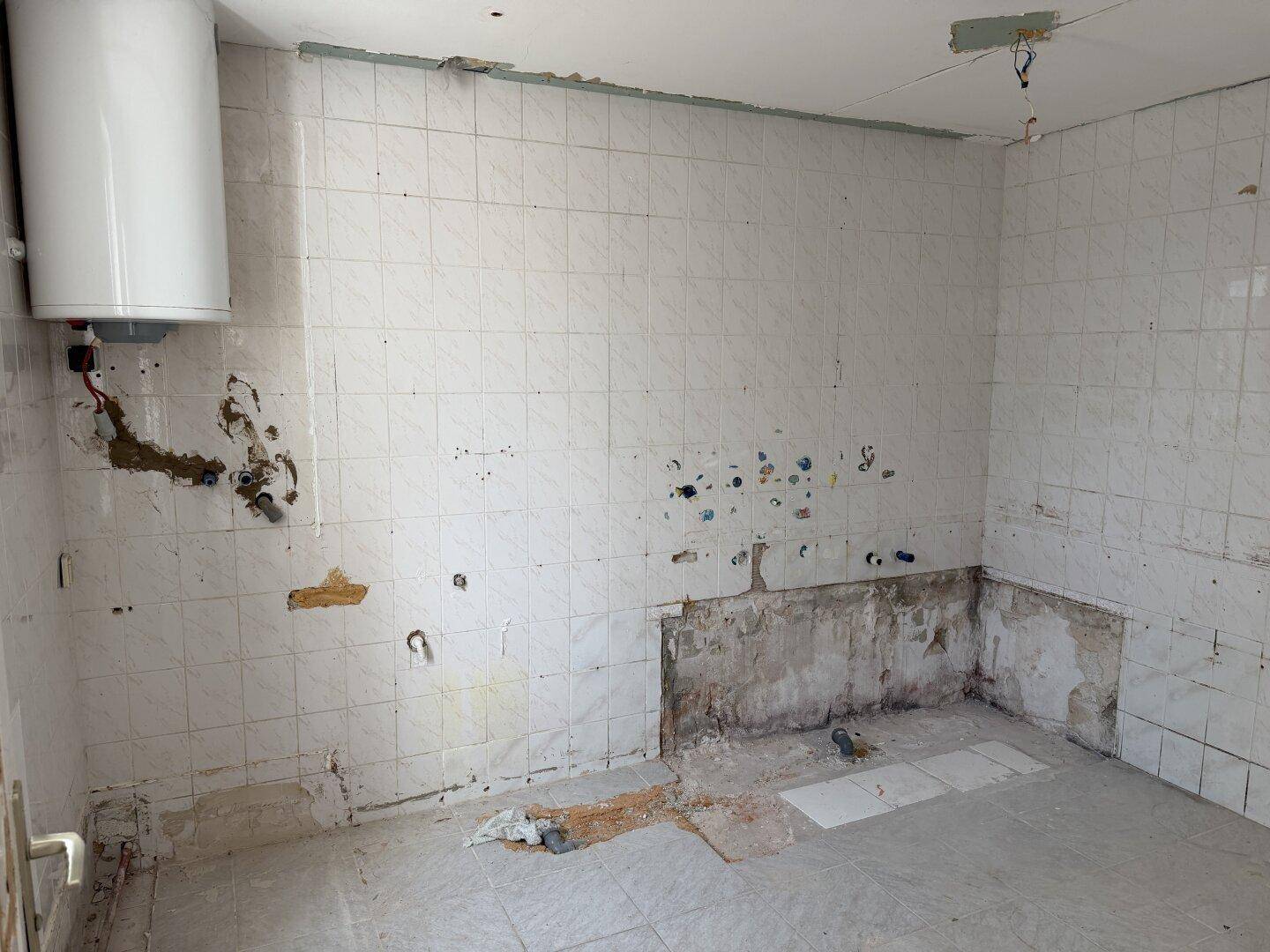 Küche im Renovierungszustand mit gefliesten Wänden und einem Warmwasserboiler.