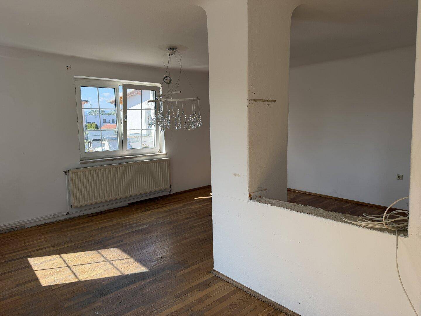 Heller Wohnraum mit Parkettboden, großem Fenster und Kronleuchter.