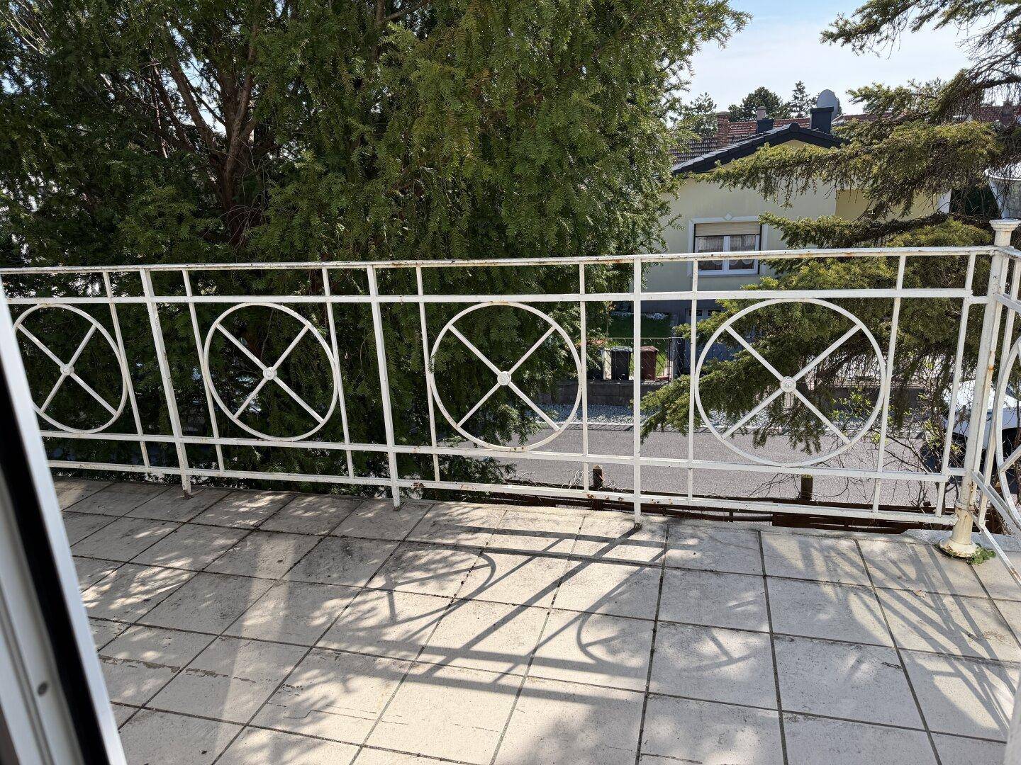 Balkon mit schmiedeeisernem Geländer und Fliesenboden, mit Blick auf die Umgebung.