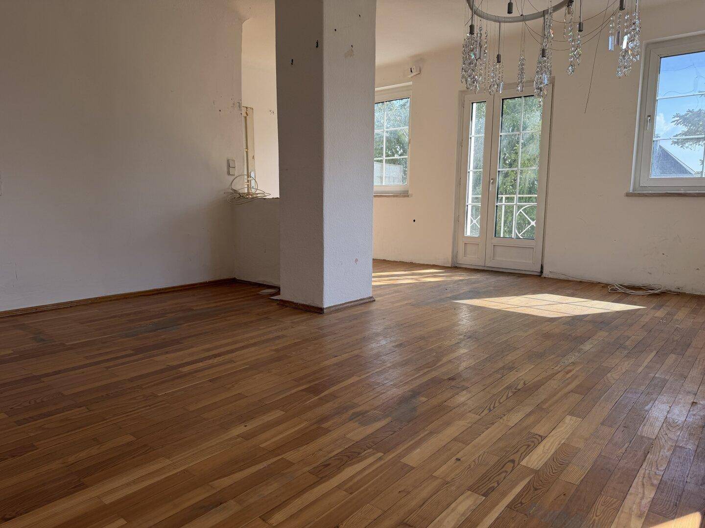 Geräumiger Wohnraum mit Parkettboden und Zugang zu einem Balkon durch eine Fenstertür.
