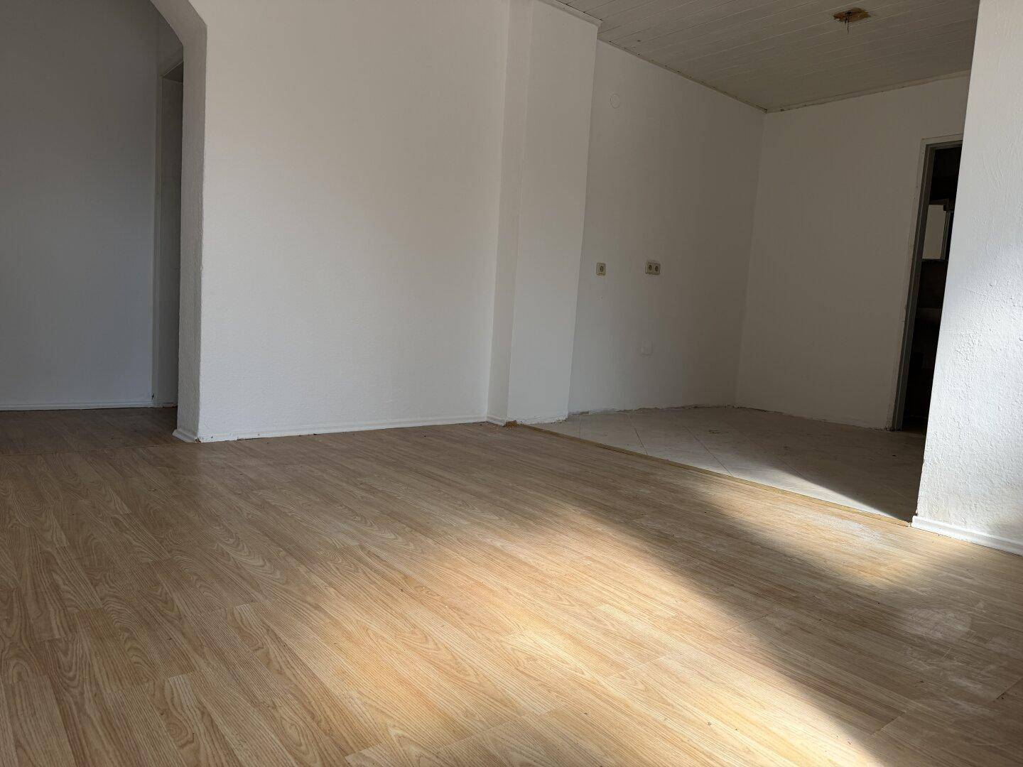 Heller Raum im Renovierungszustand mit Laminatboden und weiß gestrichenen Wänden.
