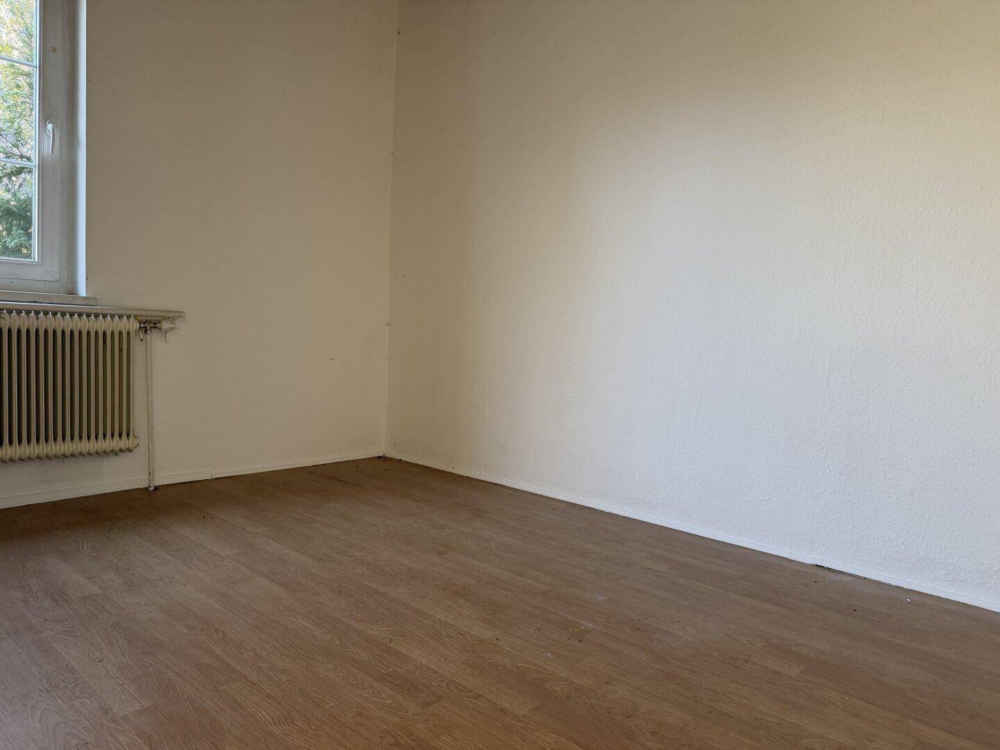 Schlafzimmer im Renovierungszustand mit Laminatboden und Heizkörper unter dem Fenster.