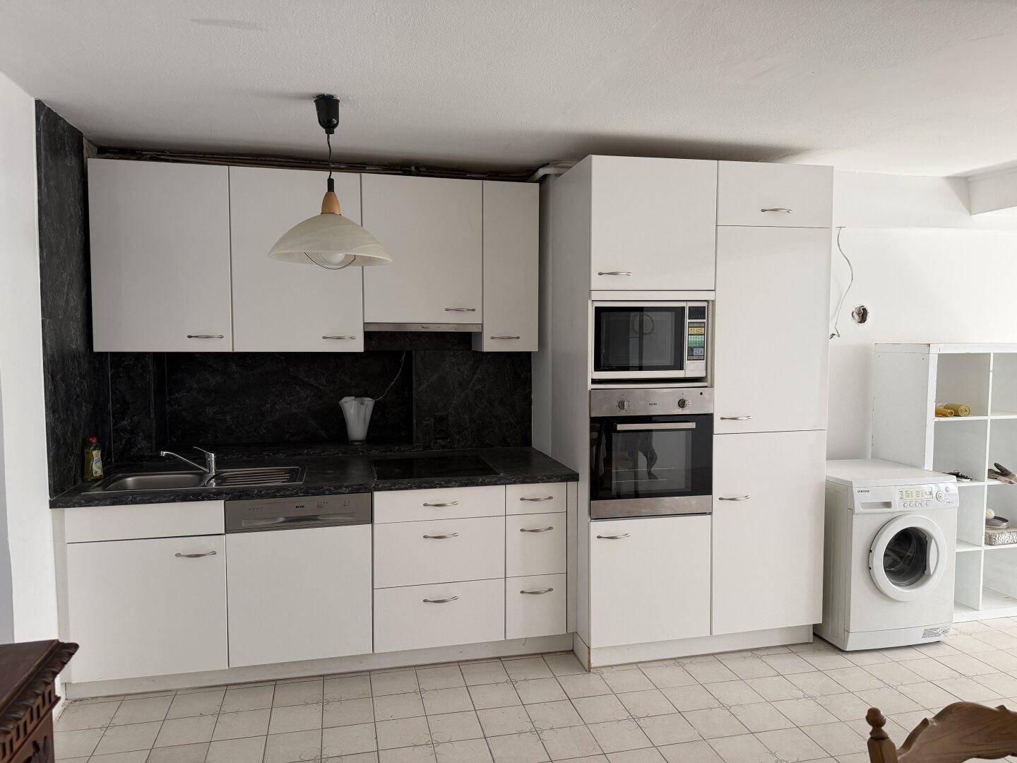 Moderne Einbauküche mit weißen Schränken, dunkler Arbeitsplatte und integrierten Geräten.