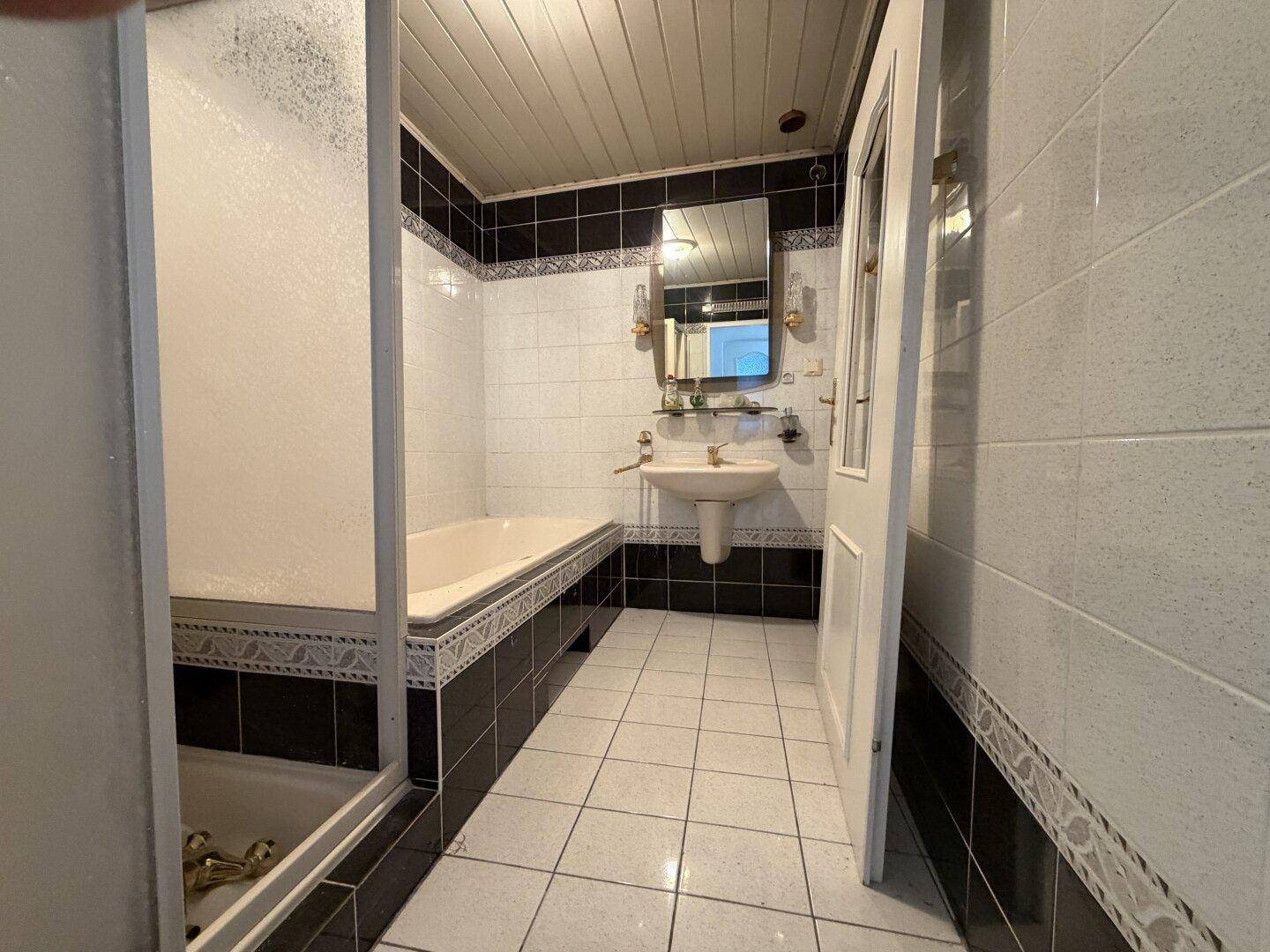 Badezimmer mit Badewanne, Waschbecken und schwarz-weißen Fliesen im 80er-Jahre-Stil.