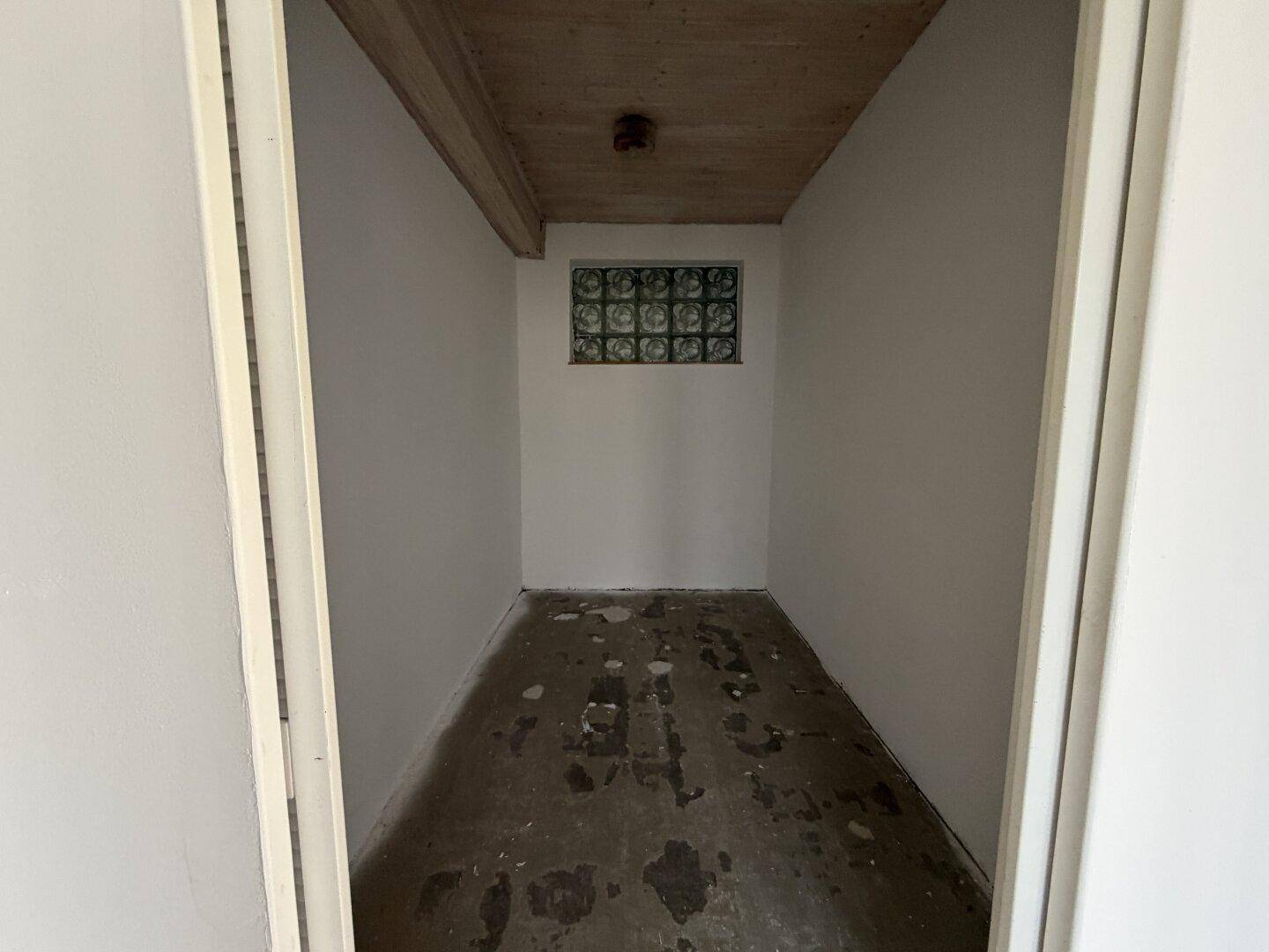 Kleiner Abstellraum mit Glasbausteinfenster und Holzbalkendecke.