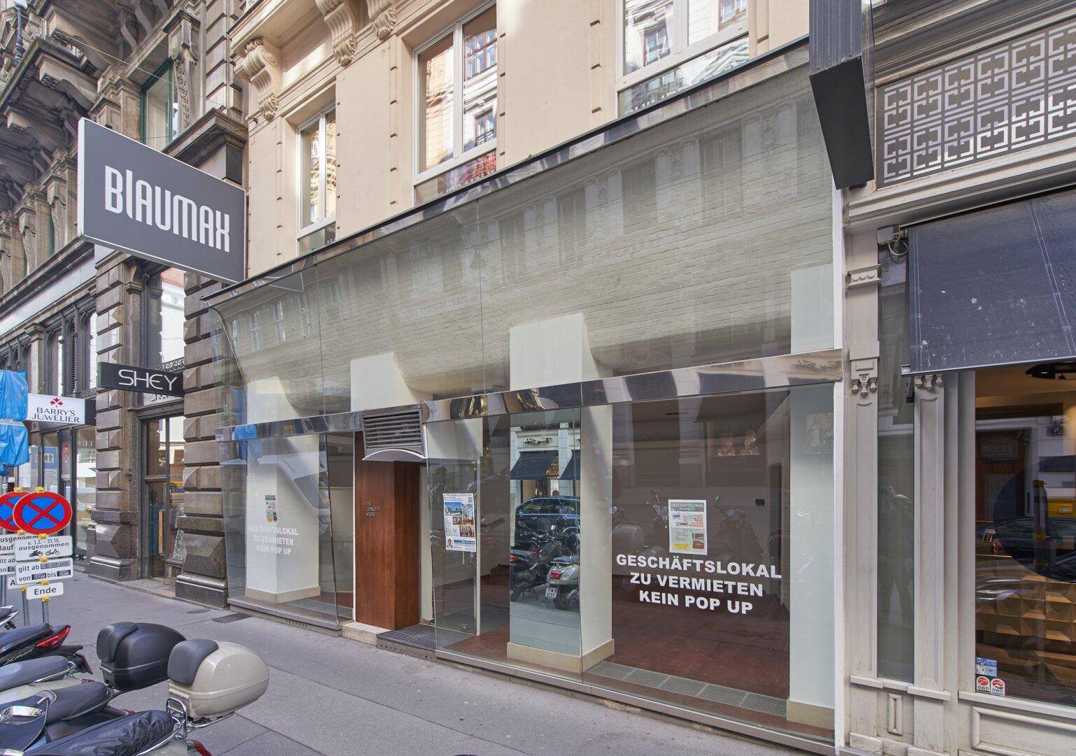 Geschäftslokal mit moderner Glasfront und angrenzenden historischen Gebäuden in urbaner Umgebung.