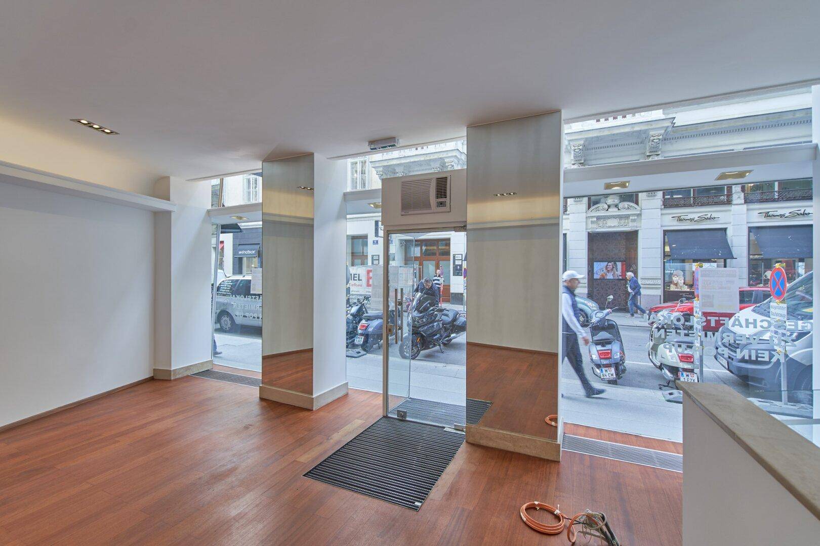 Heller Verkaufsraum mit Holzboden und großer Glasfront, die viel Tageslicht hereinlässt.