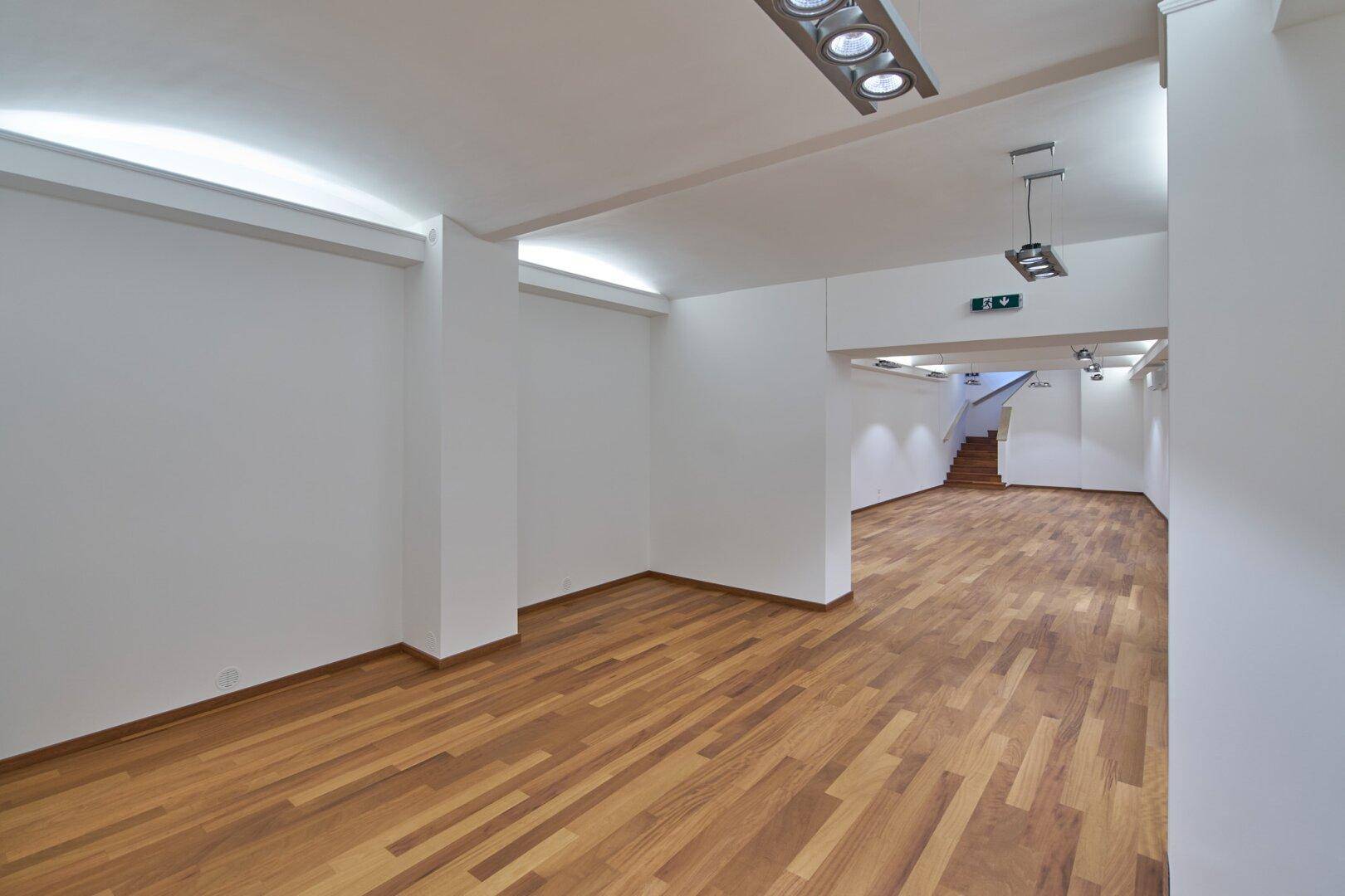 Weitläufiger, leerer Verkaufsraum mit Holzboden und moderner Deckenbeleuchtung, bereit zur Einrichtung.