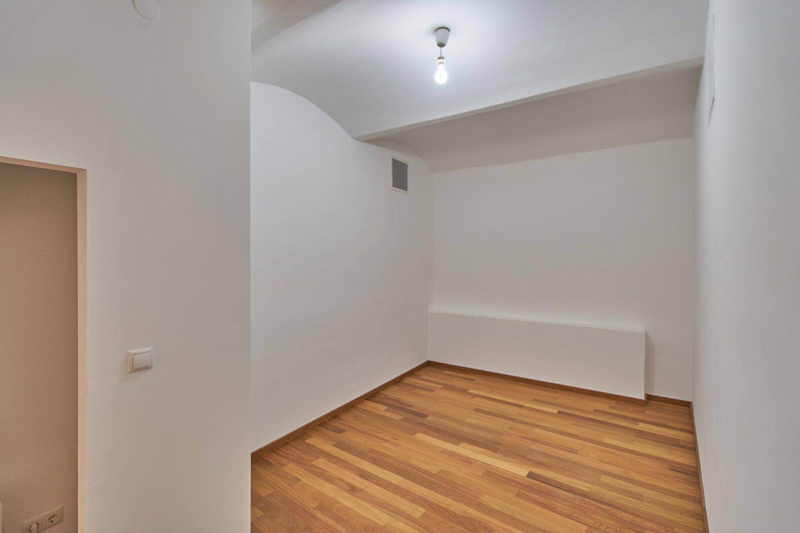 Kleiner, heller Raum mit Holzboden und weiß gestrichenen Wänden, ideal als Lager oder Büro.