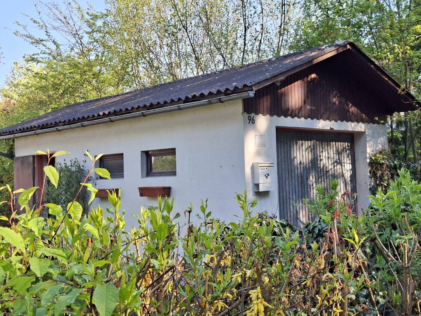 Separate Garage mit Schwingtor und kleiner Fensterfront, umgeben von Grün.