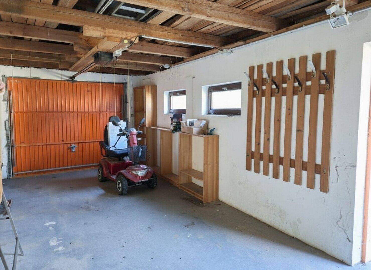 Innenansicht der Garage mit Betonboden, Holzbalken und Schwingtor.