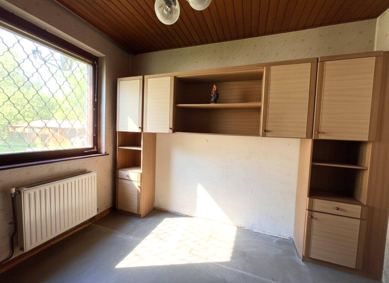 Helles Zimmer mit Einbauschränken, Holzdecke und großem Fenster.