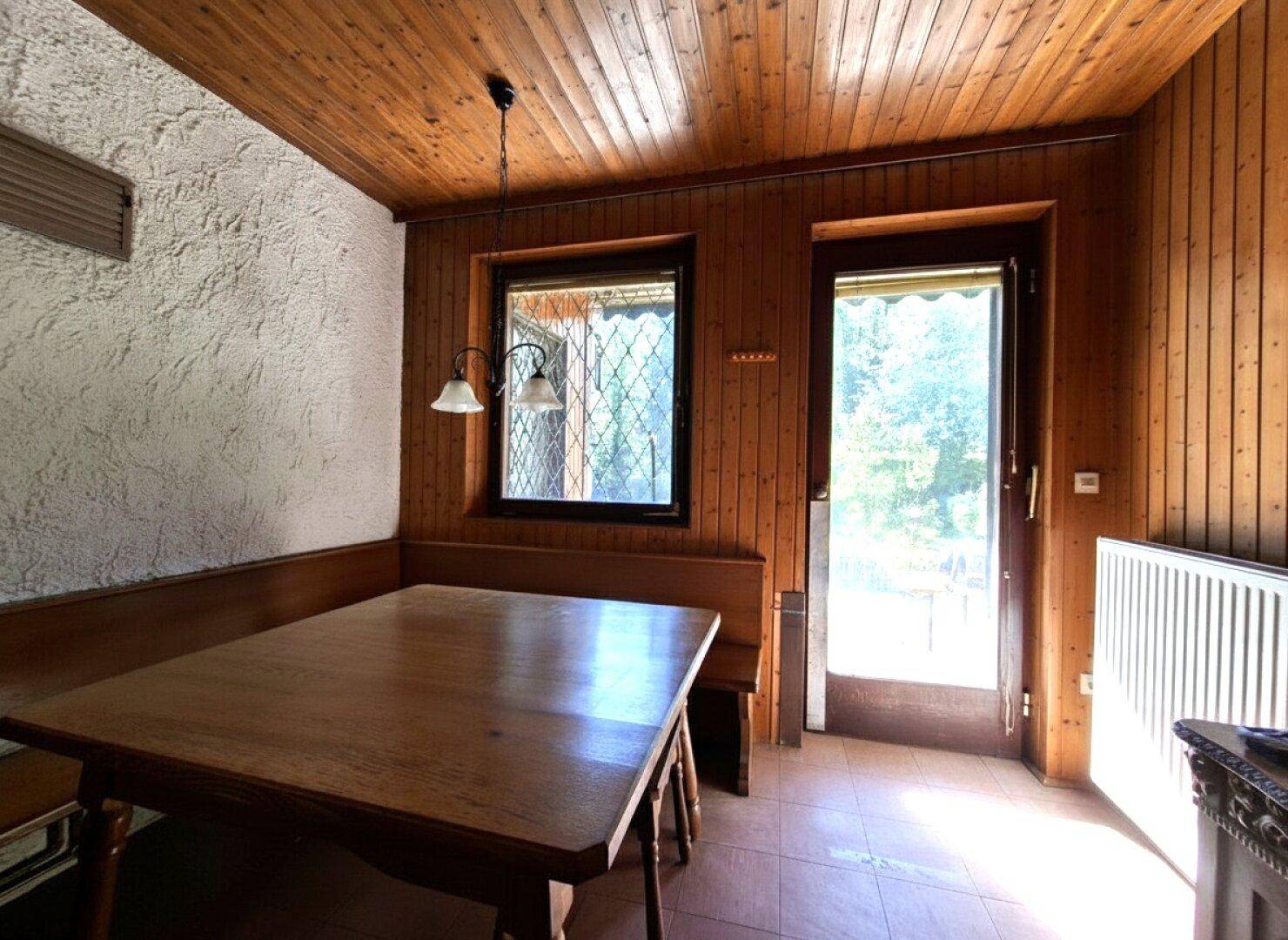 Gemütlicher Essbereich mit Holztisch, Eckbank und Holzvertäfelung an Wänden und Decke.
