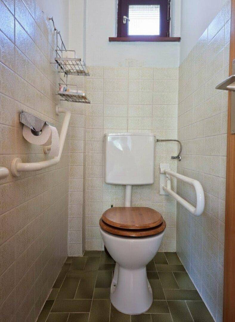 Kleines WC mit Fliesen, Fenster und Haltegriffen für Barrierefreiheit.