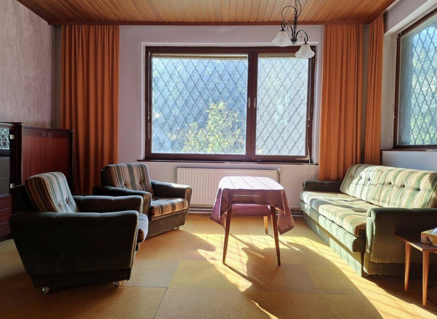 Helles Wohnzimmer mit bequemen Sitzmöbeln, Holzdecke und großem Fenster.