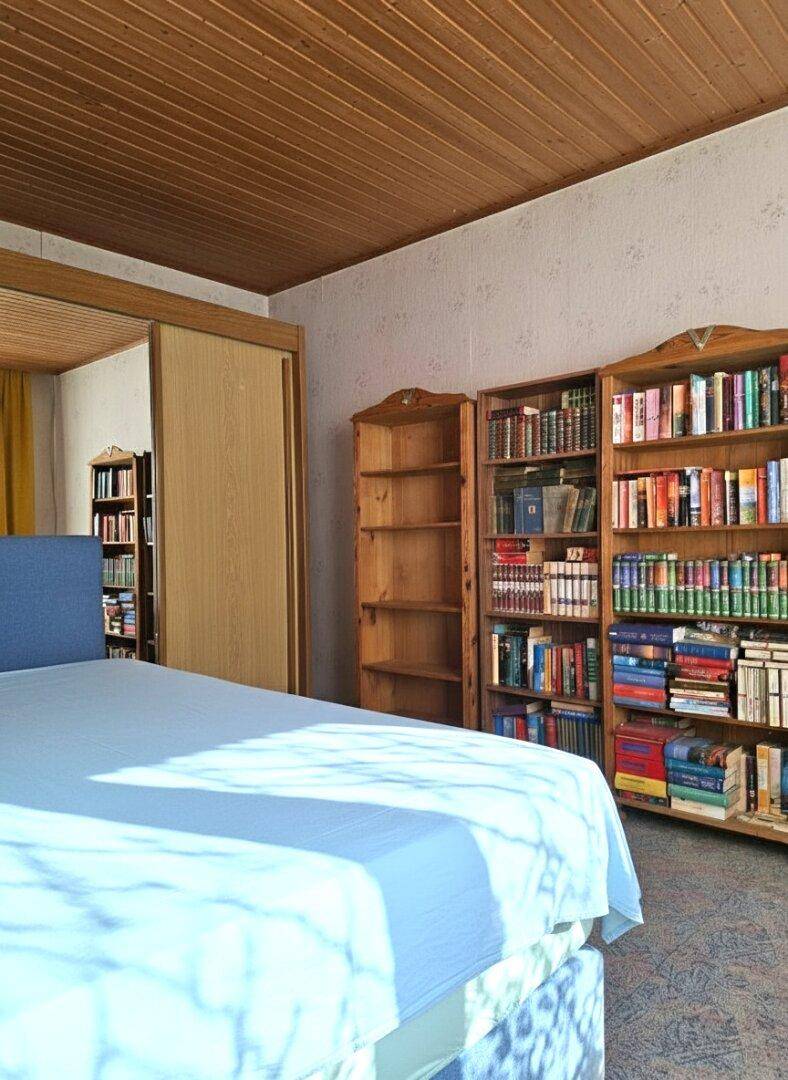 Schlafzimmer mit Bücherregalen, Holzdecke und Fenster, das viel Licht hereinlässt.