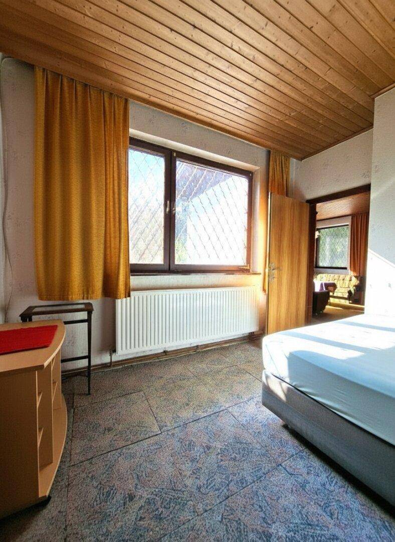 Schlafzimmer mit Fenster, Heizung und Holzdecke, hell und funktional eingerichtet.