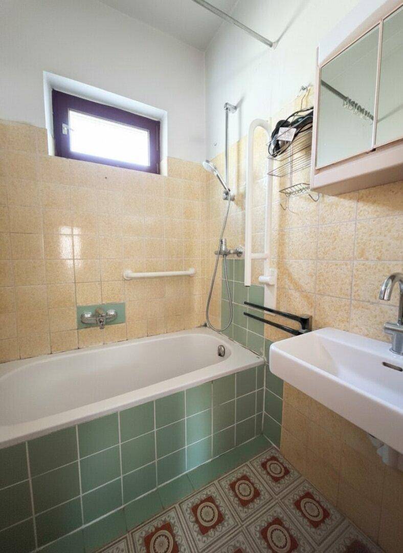 Badezimmer mit Badewanne, Waschbecken, Spiegel und farbigen Fliesen.