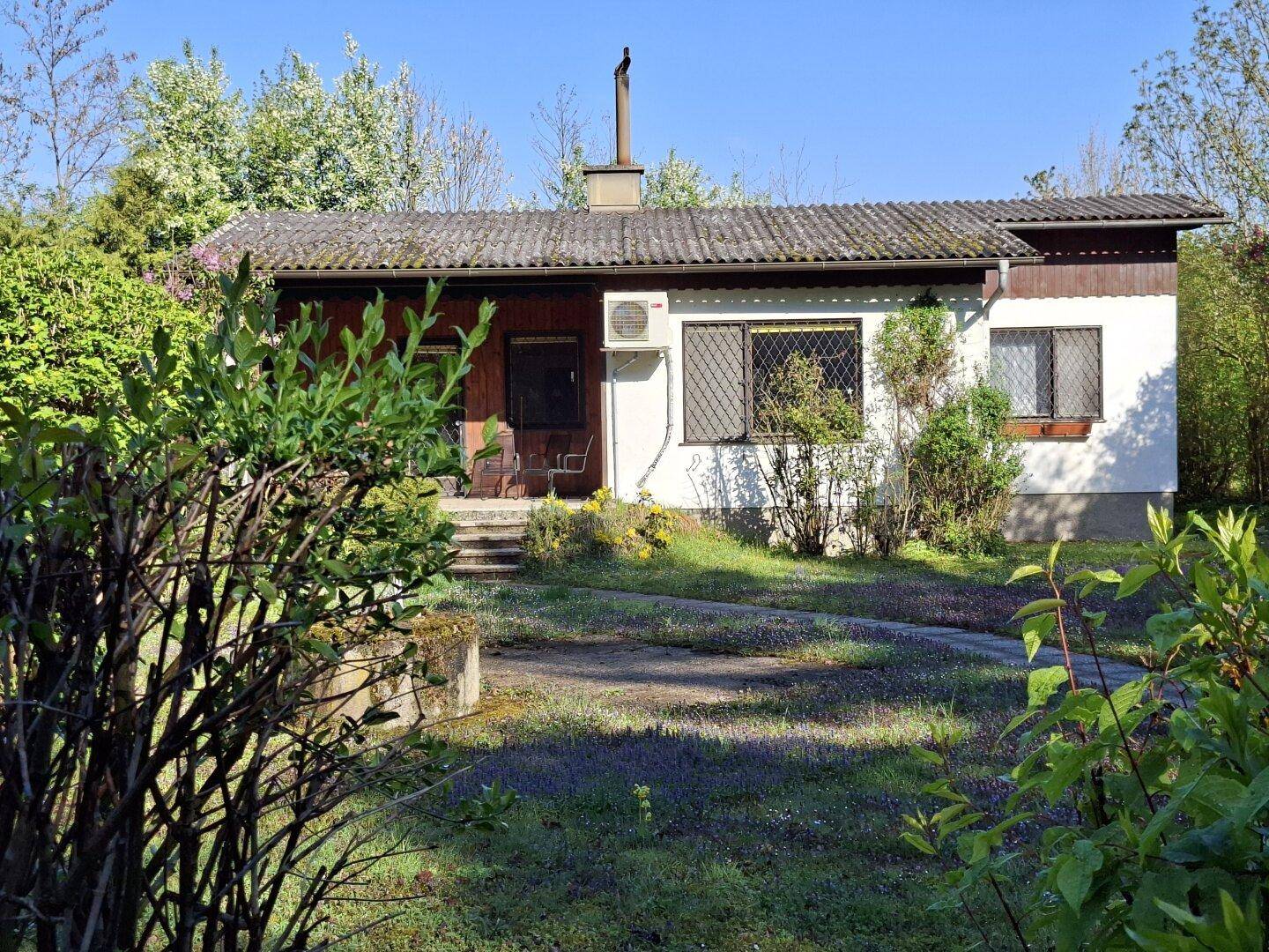 Ansicht des Hauses von vorne mit Vorgarten und Bäumen im Sonnenlicht.