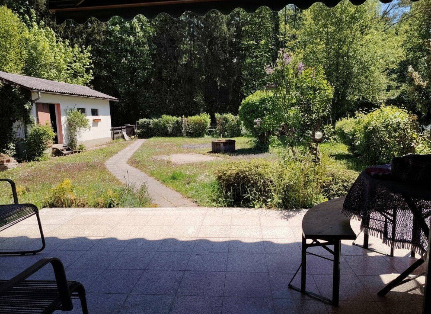 Geflieste Terrasse mit Gartenmöbeln und Blick auf den weitläufigen Gartenbereich.