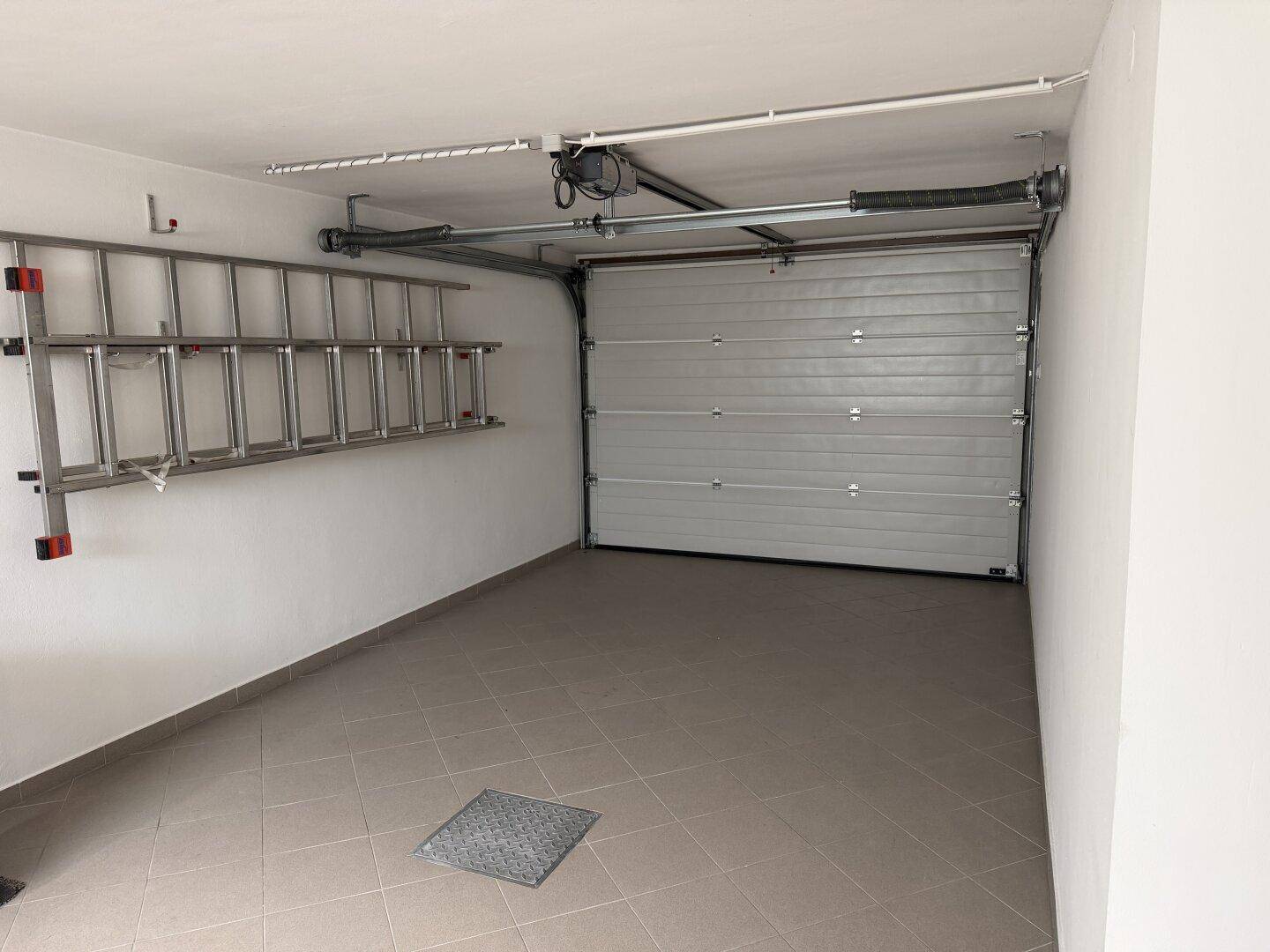 Leere Garage mit automatischem Tor und Leiter an der Wand.