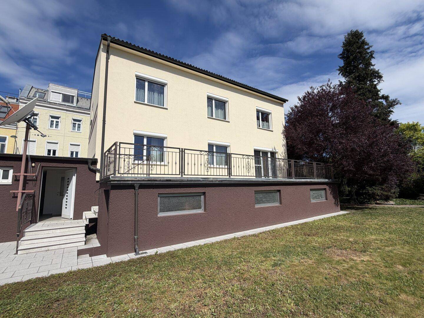 Gesamtansicht des Hauses mit heller Fassade, mehreren Fenstern und einem Balkon mit Geländer.