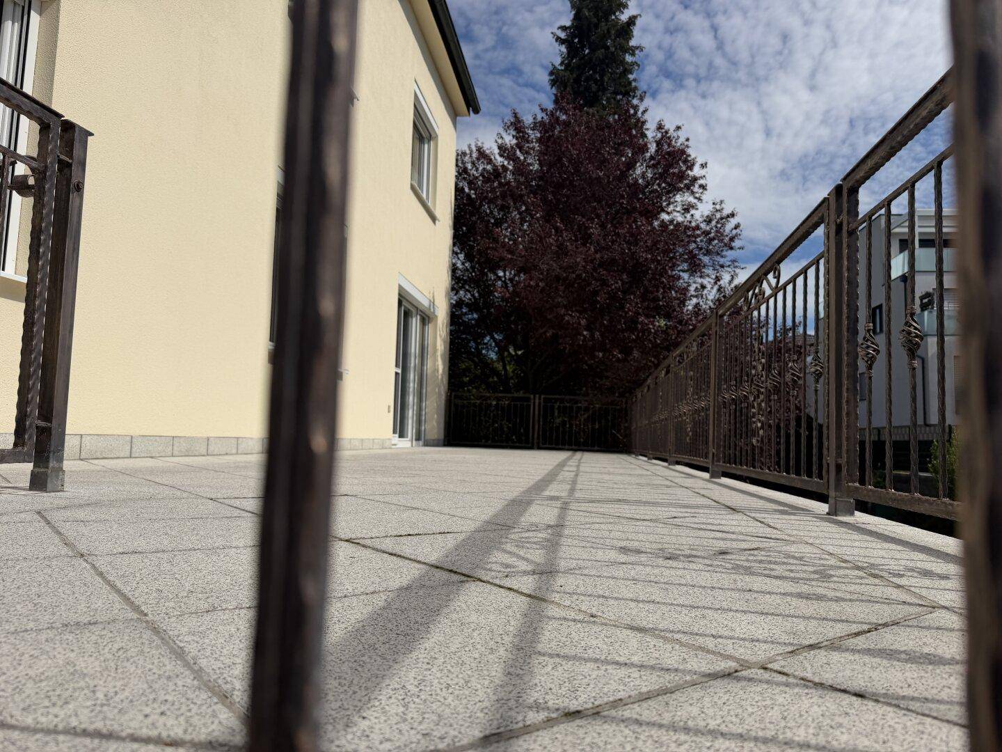 Große, geflieste Terrasse mit schmiedeeisernem Geländer und Blick auf die Hausfassade.