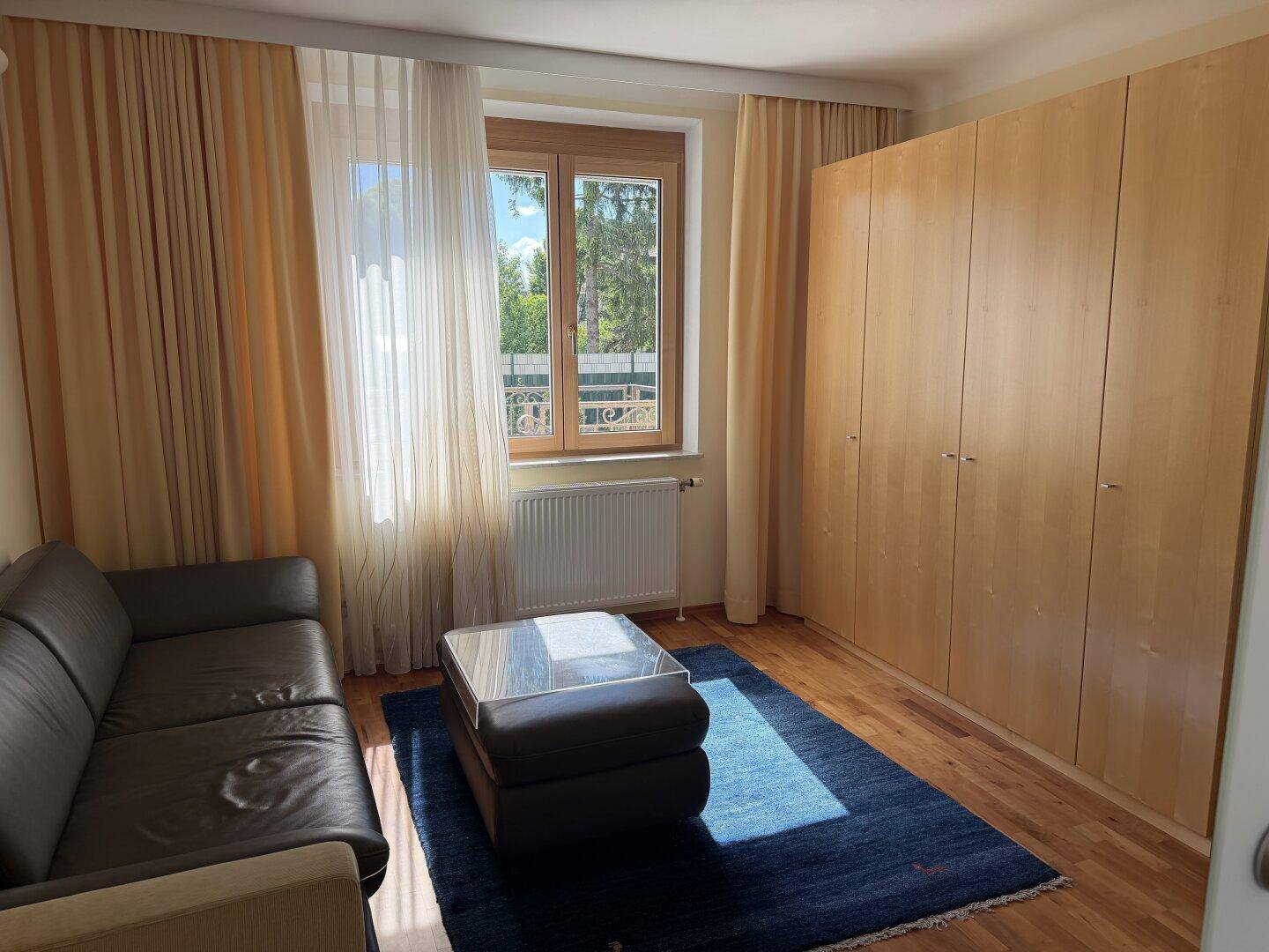 Schlafzimmer mit dunklem Ledersofa, Holzboden und großem Kleiderschrank.