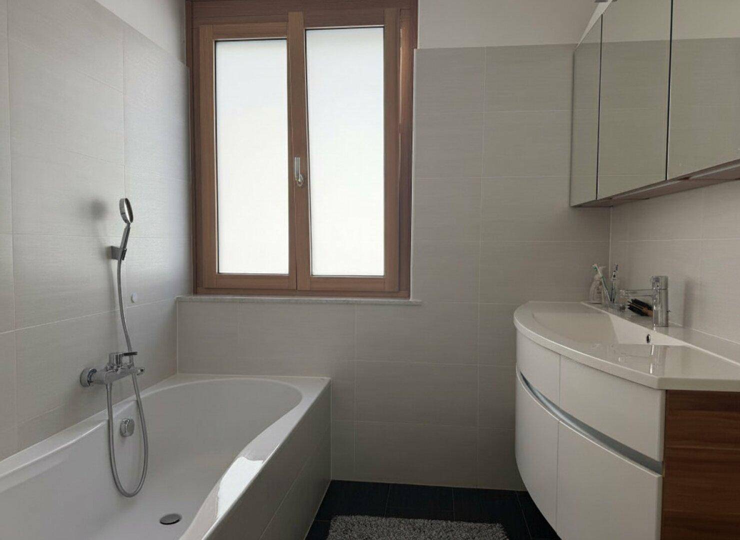 Modernes Badezimmer mit Badewanne, Waschtisch und Fenster für natürliche Belüftung.