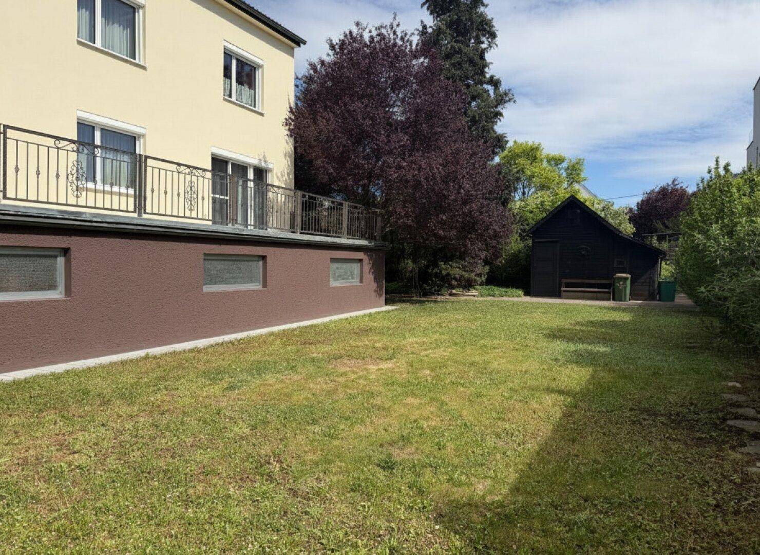 Großer Garten mit Rasenfläche, Bäumen und einem Gartenhaus im Hintergrund.