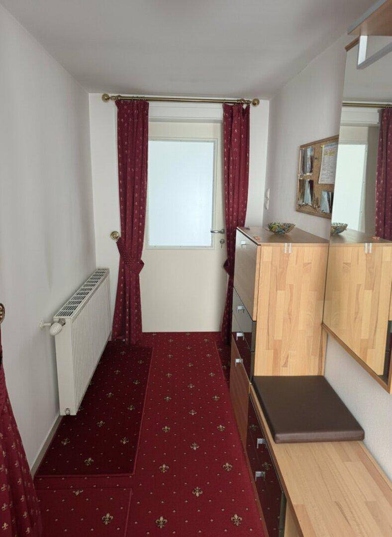 Schmaler Flur mit rotem Teppich, Garderobe und Fenster an der Eingangstür.