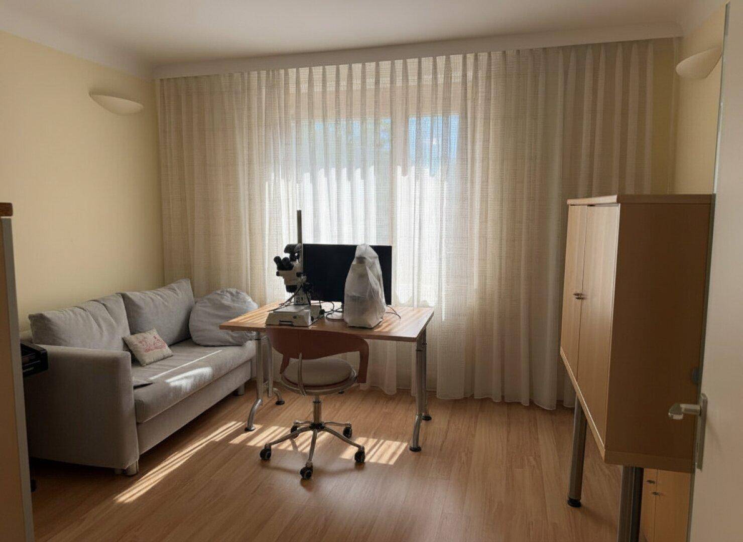 Helles Zimmer mit Sofa, Schreibtisch und großem Fenster, ideal als Arbeits- oder Gästezimmer.