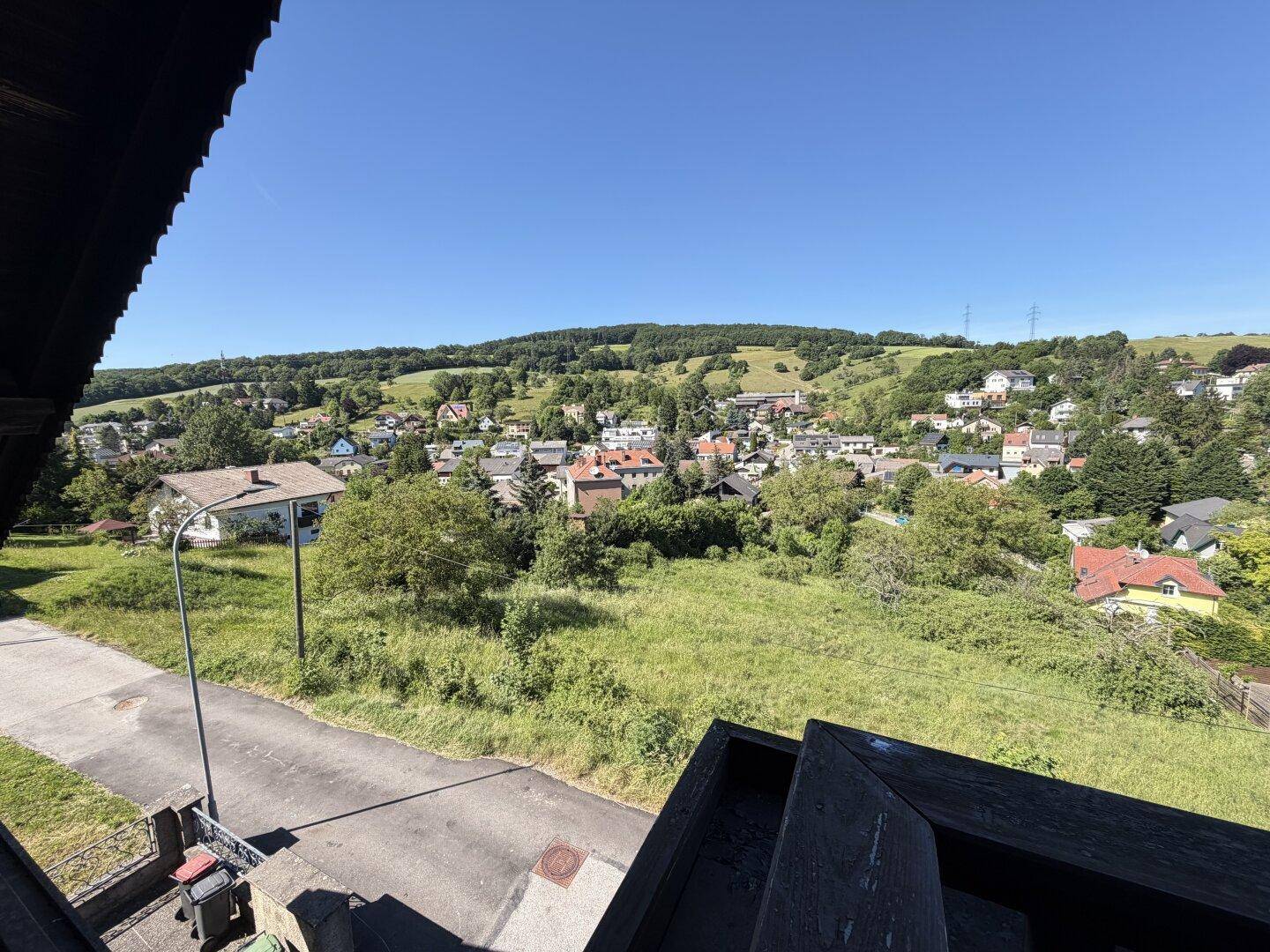 Weitläufiger Blick von der Anhöhe über das Dorf und die grüne, hügelige Landschaft.
