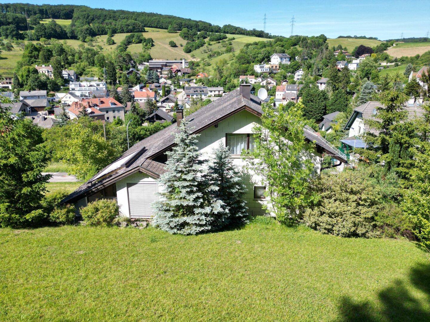 Haus in Hanglage mit weitem Blick über das Dorf und die umliegende grüne Hügellandschaft.