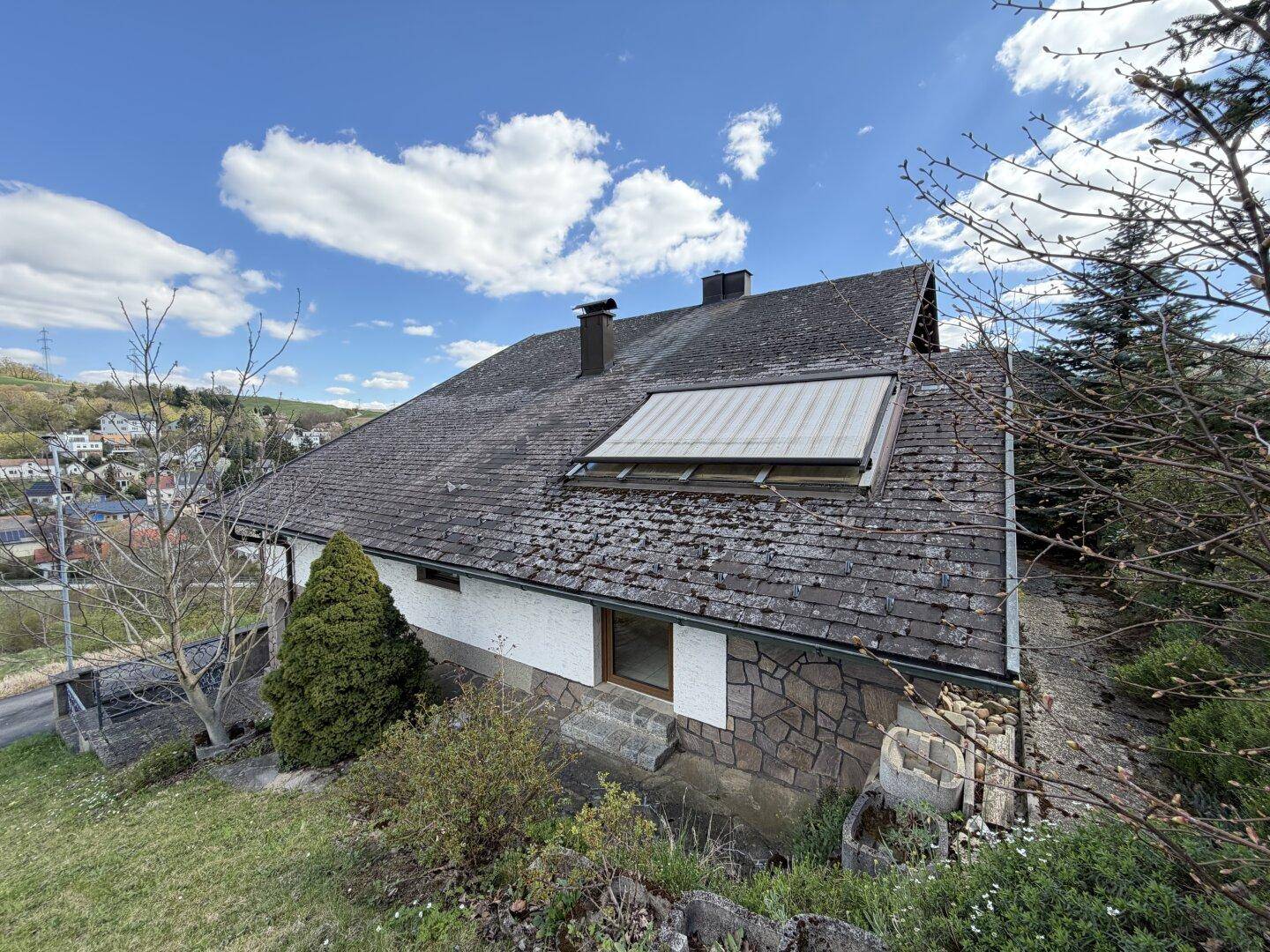 Seitenansicht des Hauses mit Satteldach und Dachfenstern, umgeben von grüner Natur.