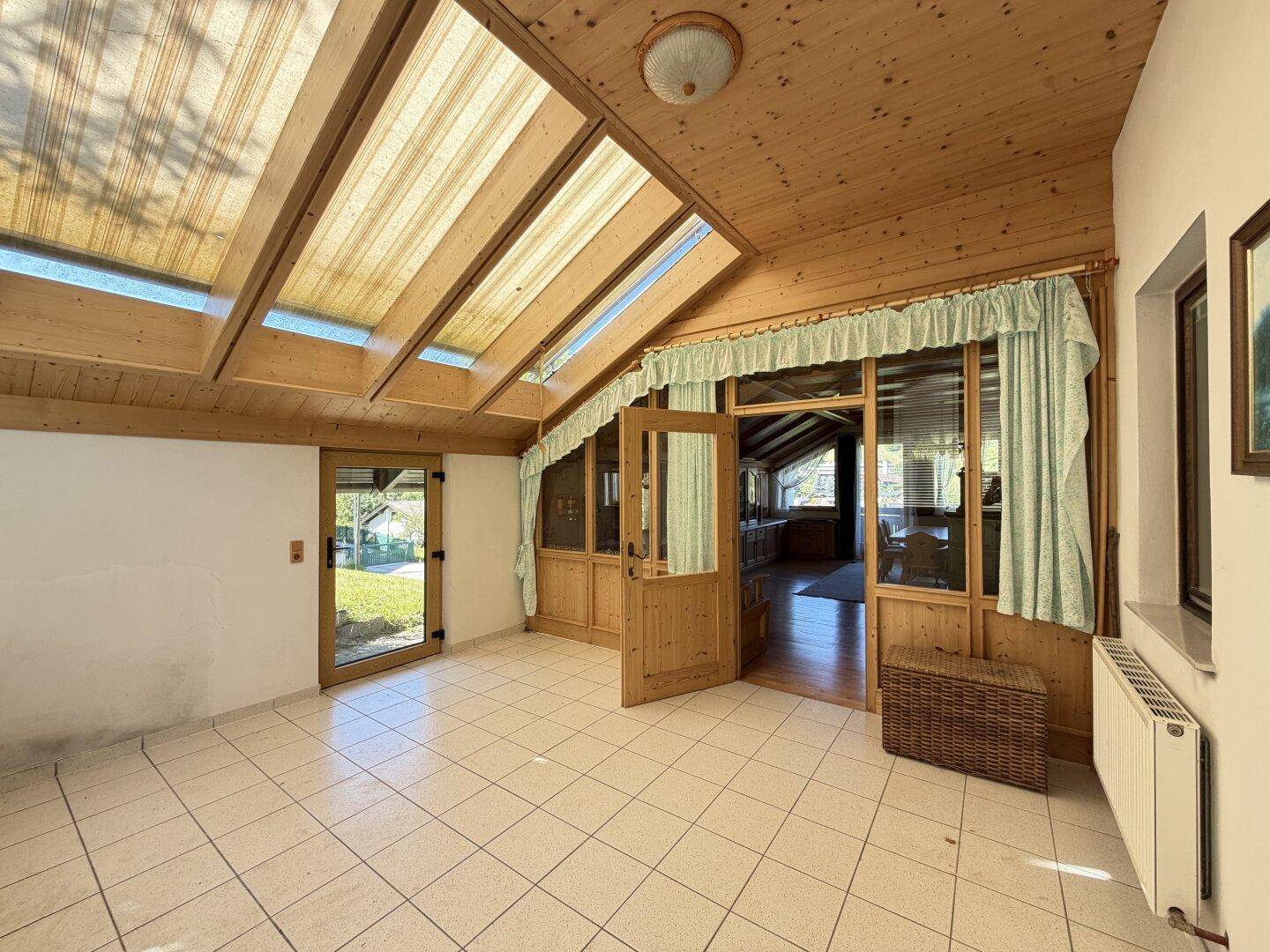 Heller Wintergarten mit Fliesenboden, Holzverkleidung und großen Dachfenstern für viel Tageslicht.