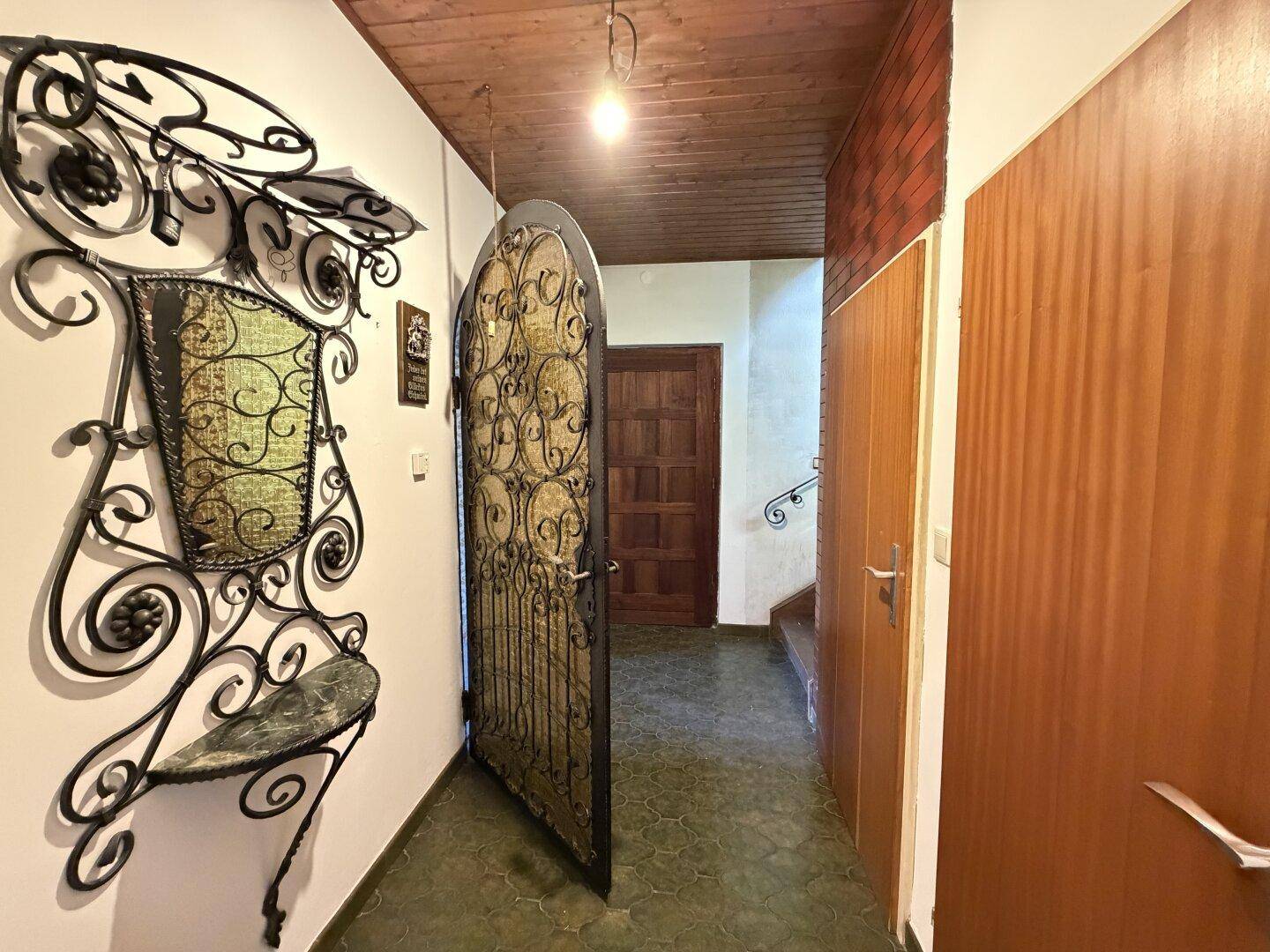 Eingangsbereich mit schmiedeeisernem Tor, Holztüren und Fliesenboden im traditionellen Stil.