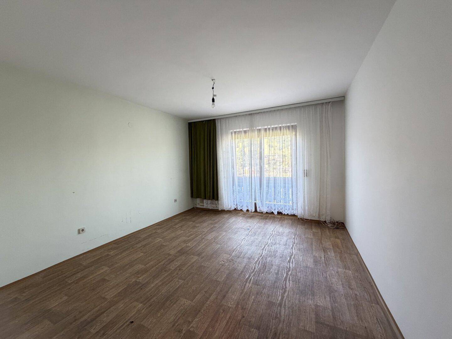 Leeres Zimmer mit Laminatboden und großem Fenster, bereit für individuelle Gestaltung.