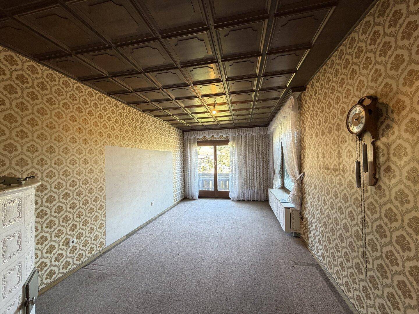 Geräumiges Zimmer mit gemusterter Tapete, Kassettendecke und Zugang zu einem Balkon.