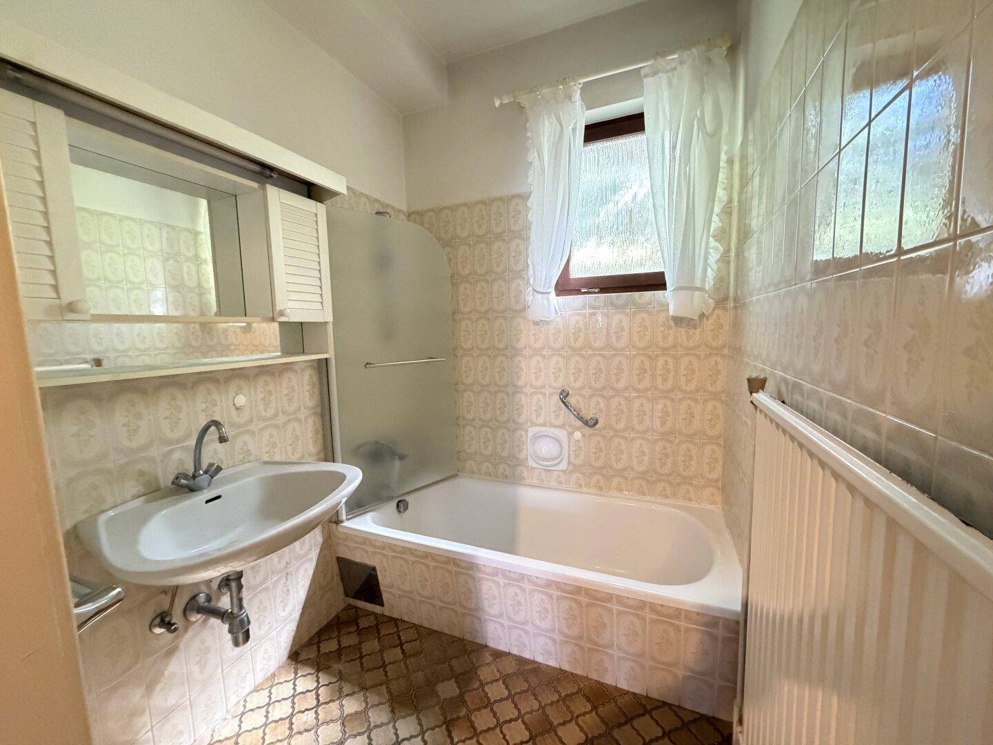 Badezimmer im 80er-Jahre-Stil mit Badewanne, Waschbecken und gemusterten Fliesen.