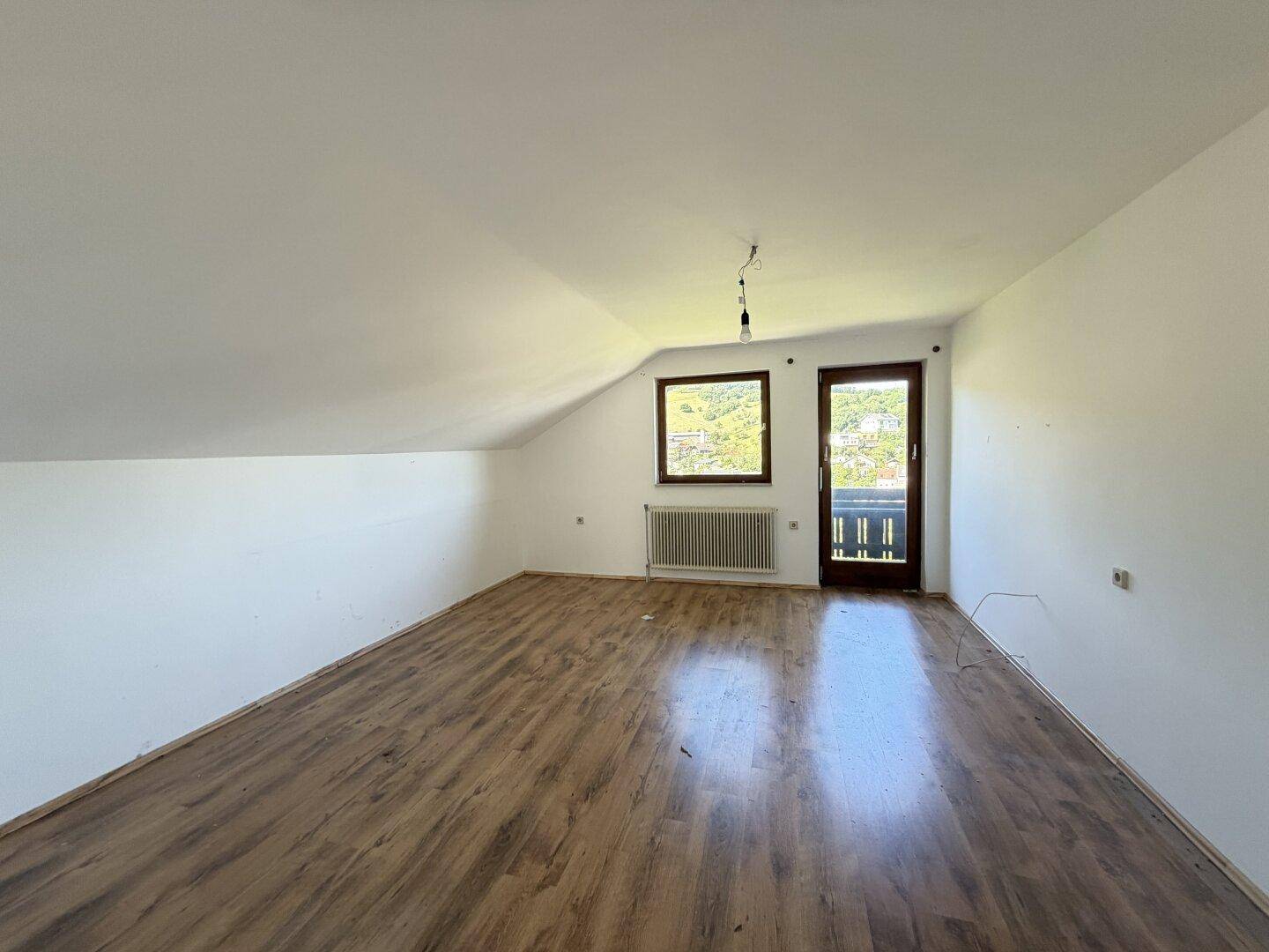 Helles Zimmer im Dachgeschoss mit Laminatboden, schrägen Wänden und Zugang zu einem Balkon.