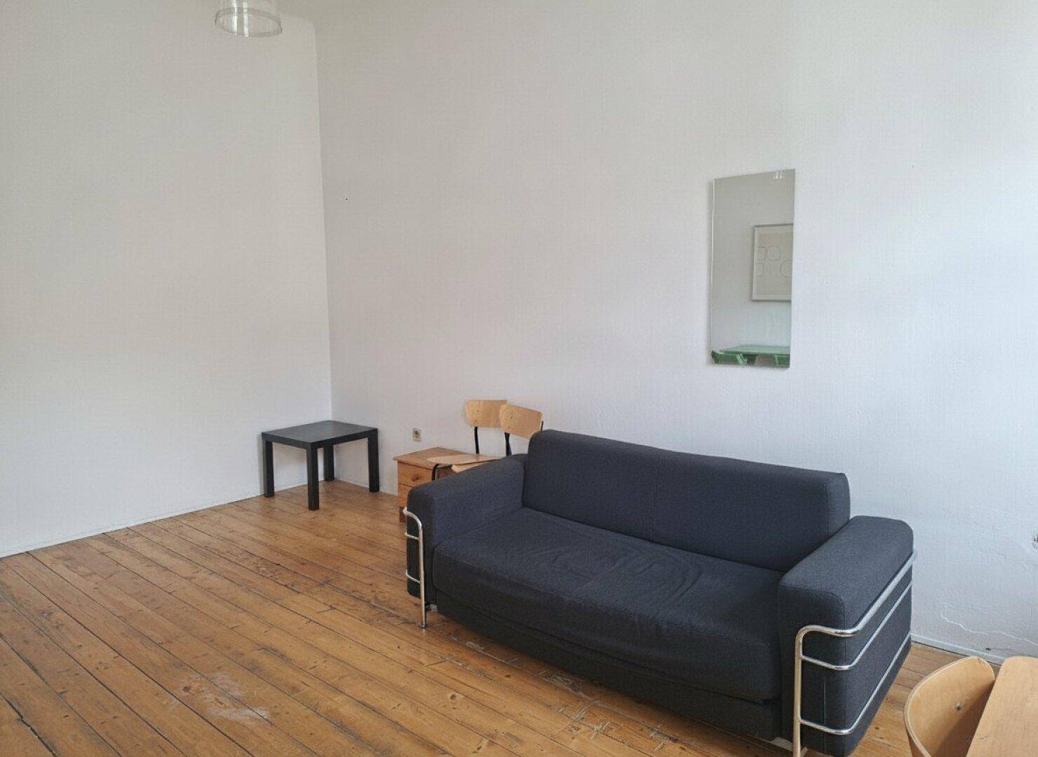 Einfaches Wohnzimmer mit Holzdielenboden und einem dunklen Sofa.