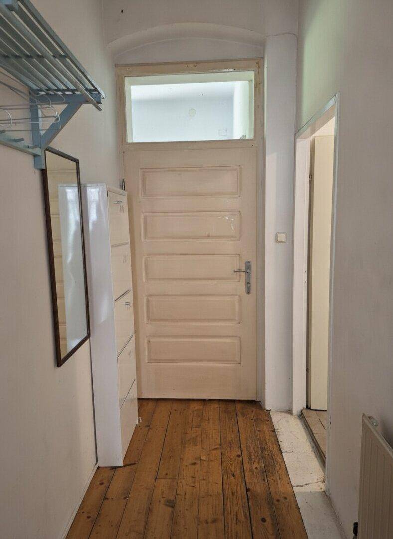 Eingangsbereich mit Holzdielenboden, alter Tür und einem Schuhschrank in einem Altbau.