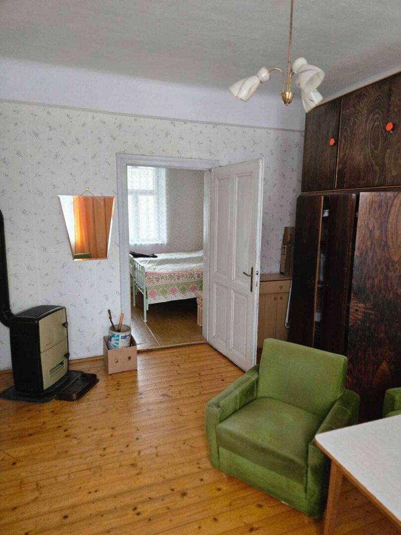 Gemütliches Wohnzimmer mit Holzofen, grünen Sesseln und Blick in ein Schlafzimmer.